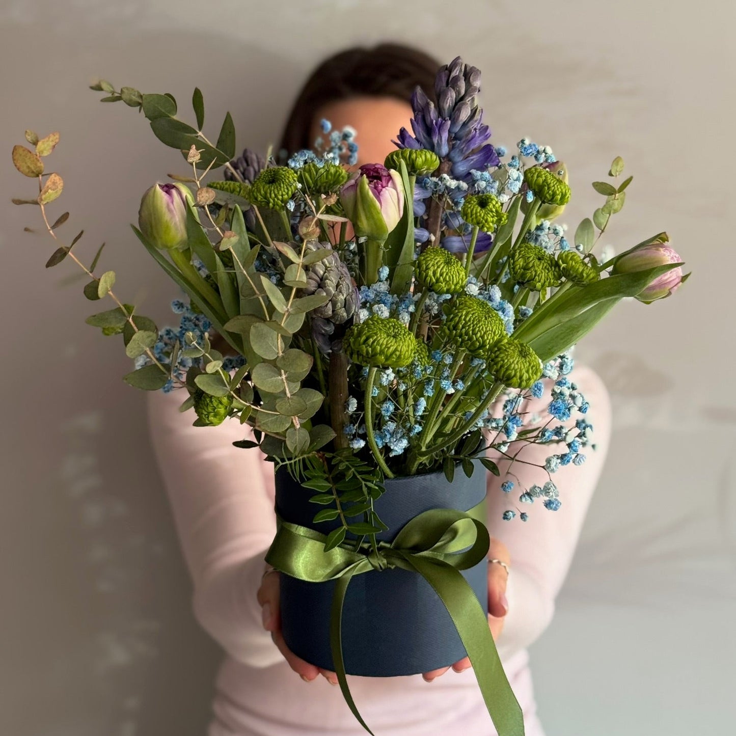 Person holding a bouquet of flowers in front of their face against a plain background