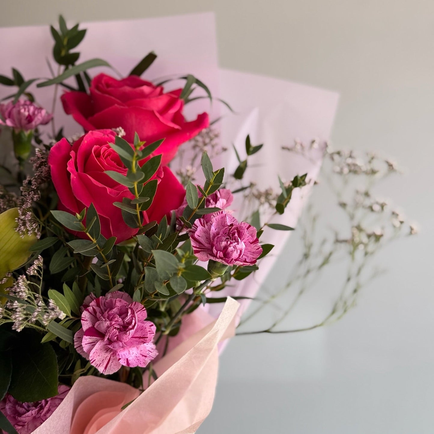 Bouquet of red and pink roses with greenery on a light background