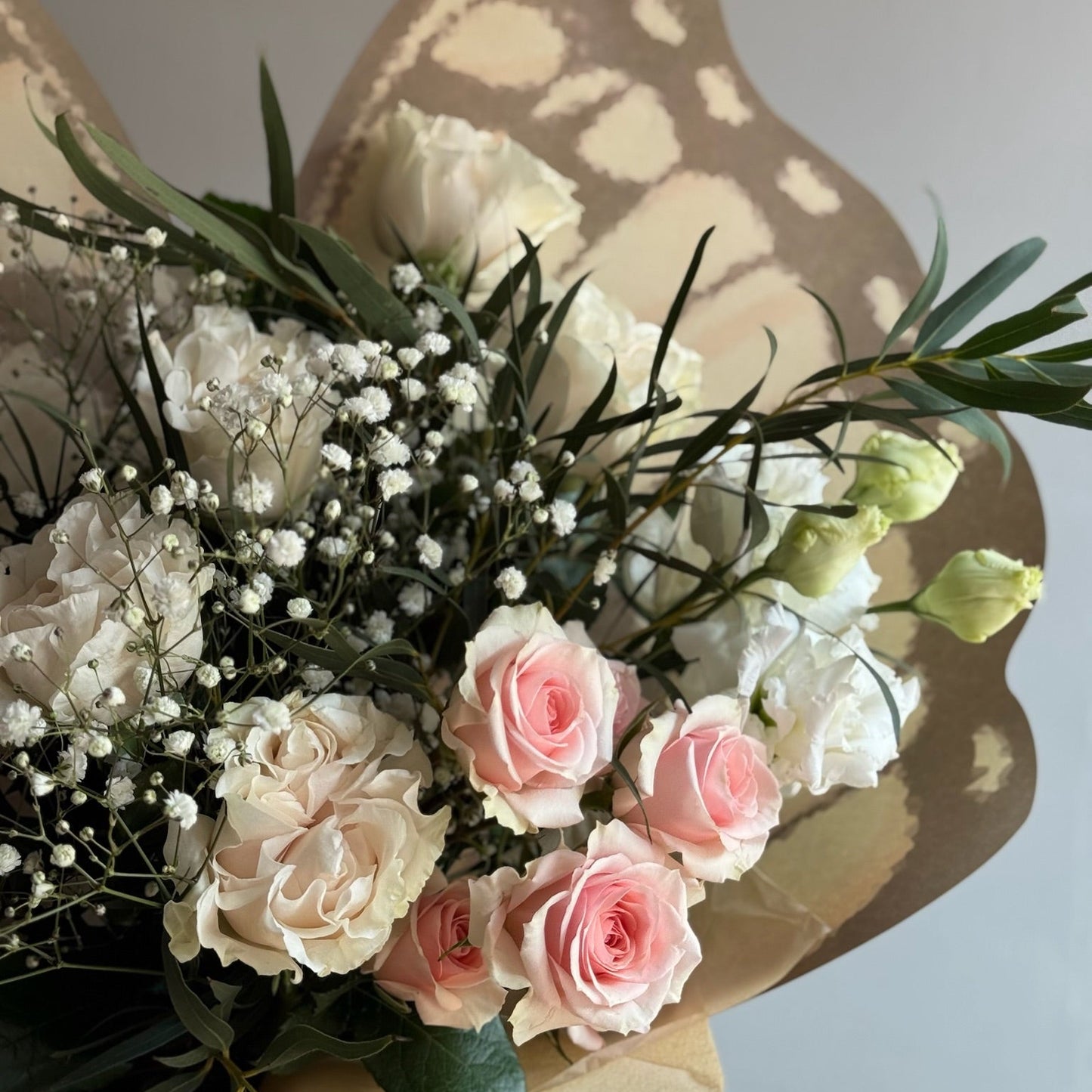 Bouquet of pink and white roses with greenery against a neutral background