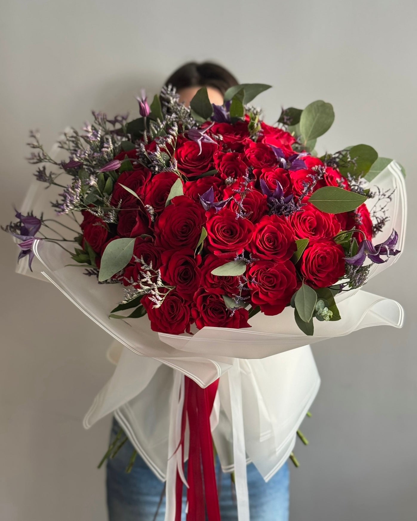 Big bouquet with red roses and white wrapping paper held on grey background