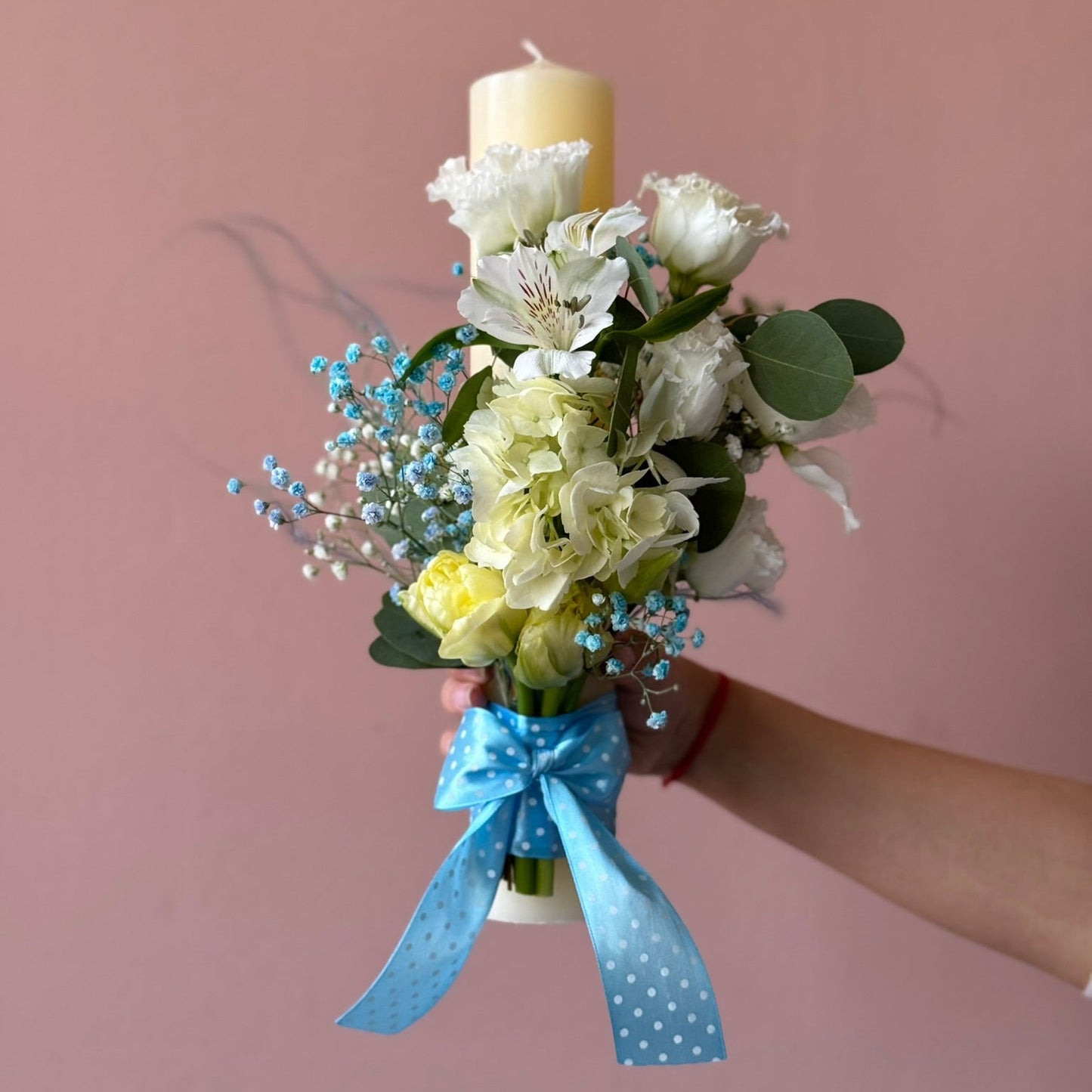 Decorative candle holder with flowers and a blue ribbon against a pink background