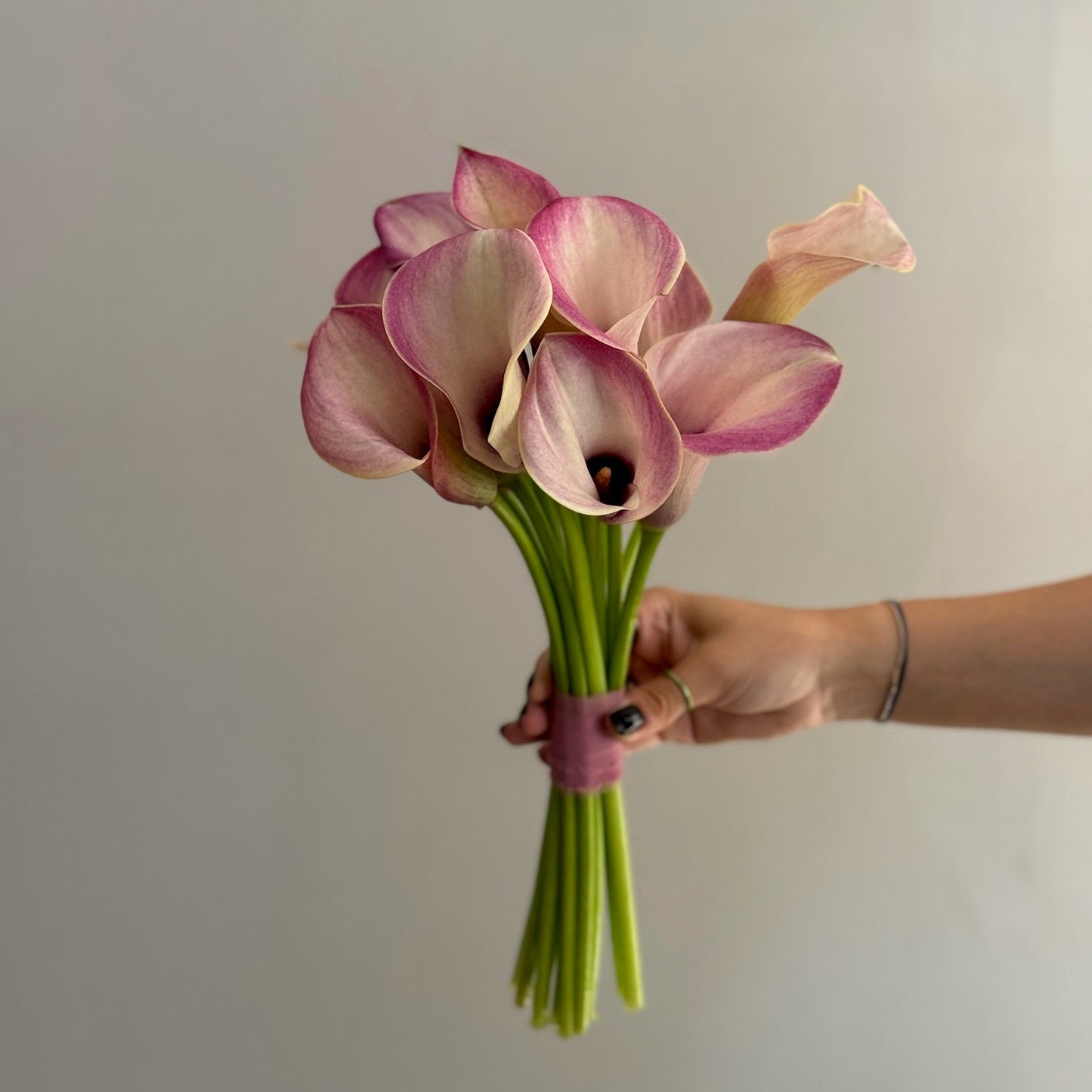 Hand holding a bouquet of pink and white flowers against a plain background