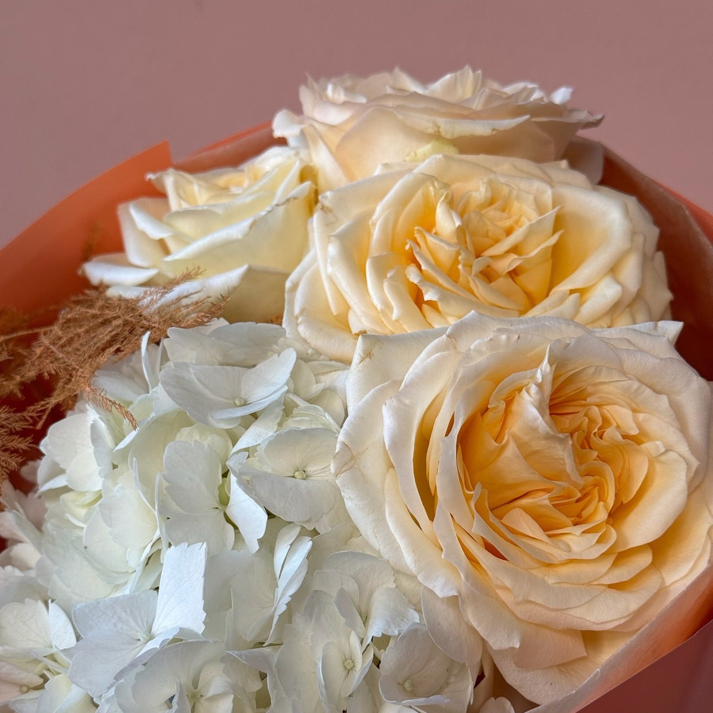 Bouquet of white and light yellow roses in a pink container.