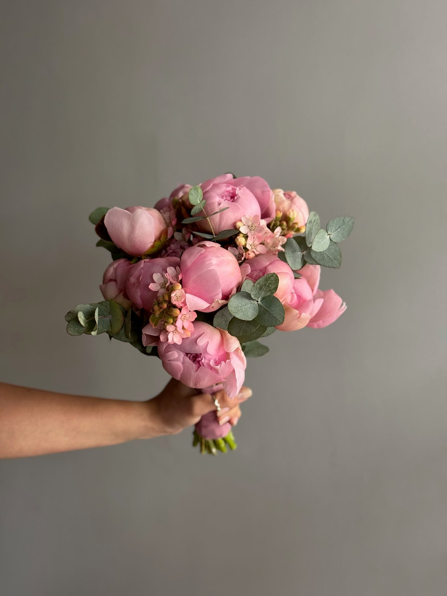 Bouquet of pink flowers held by a person against a gray background