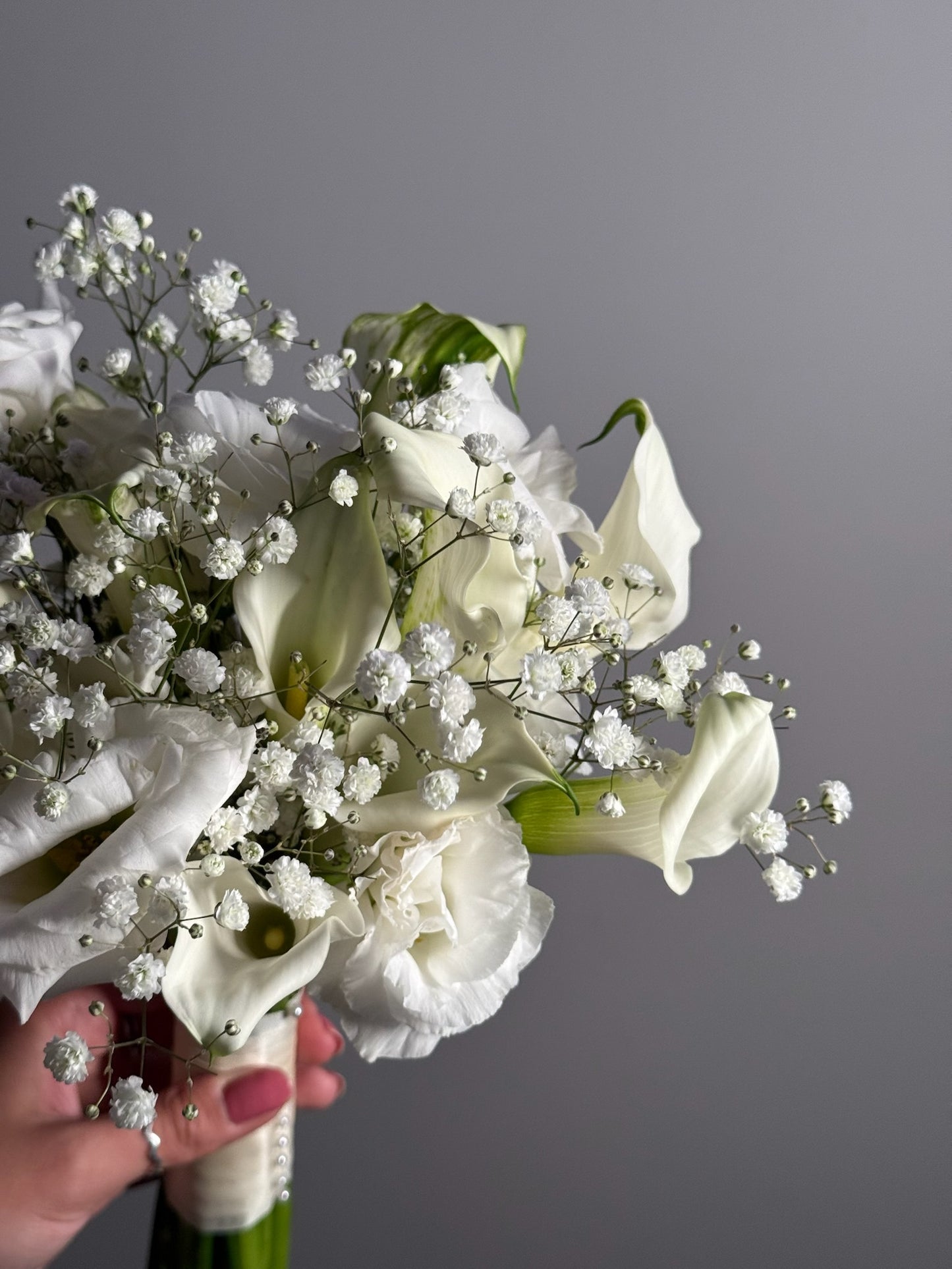 Bouquet of white flowers held by a hand against a gray background