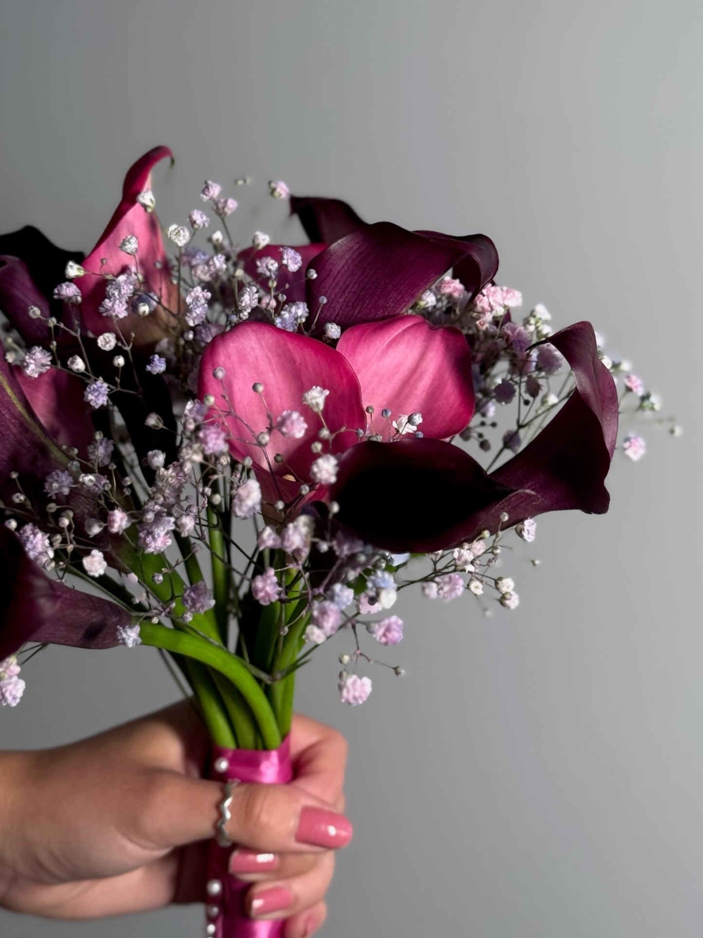 Bouquet of purple calla lilies with baby's breath held by a hand against a gray background