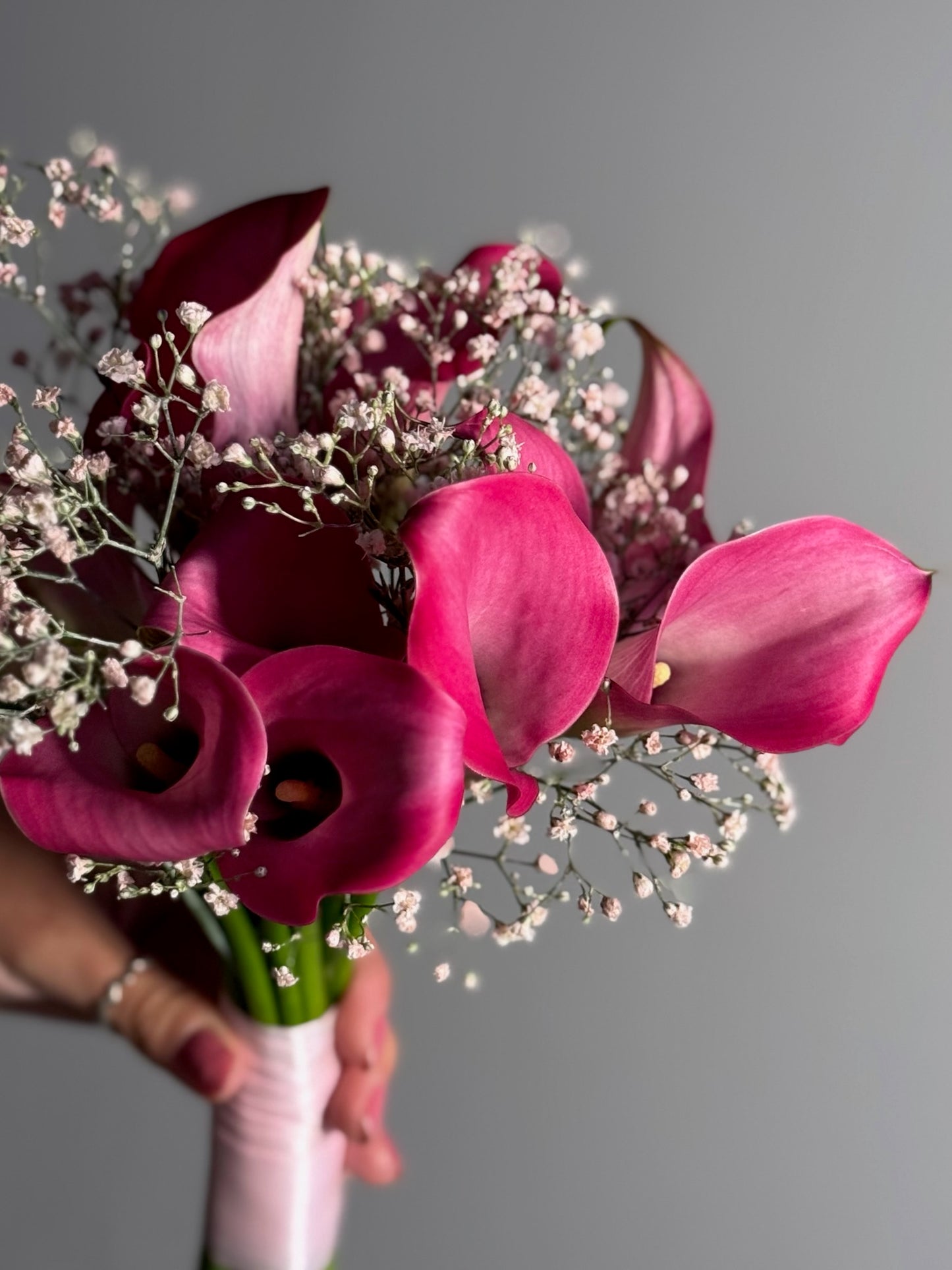 Bouquet of pink and purple flowers held by a person against a gray background