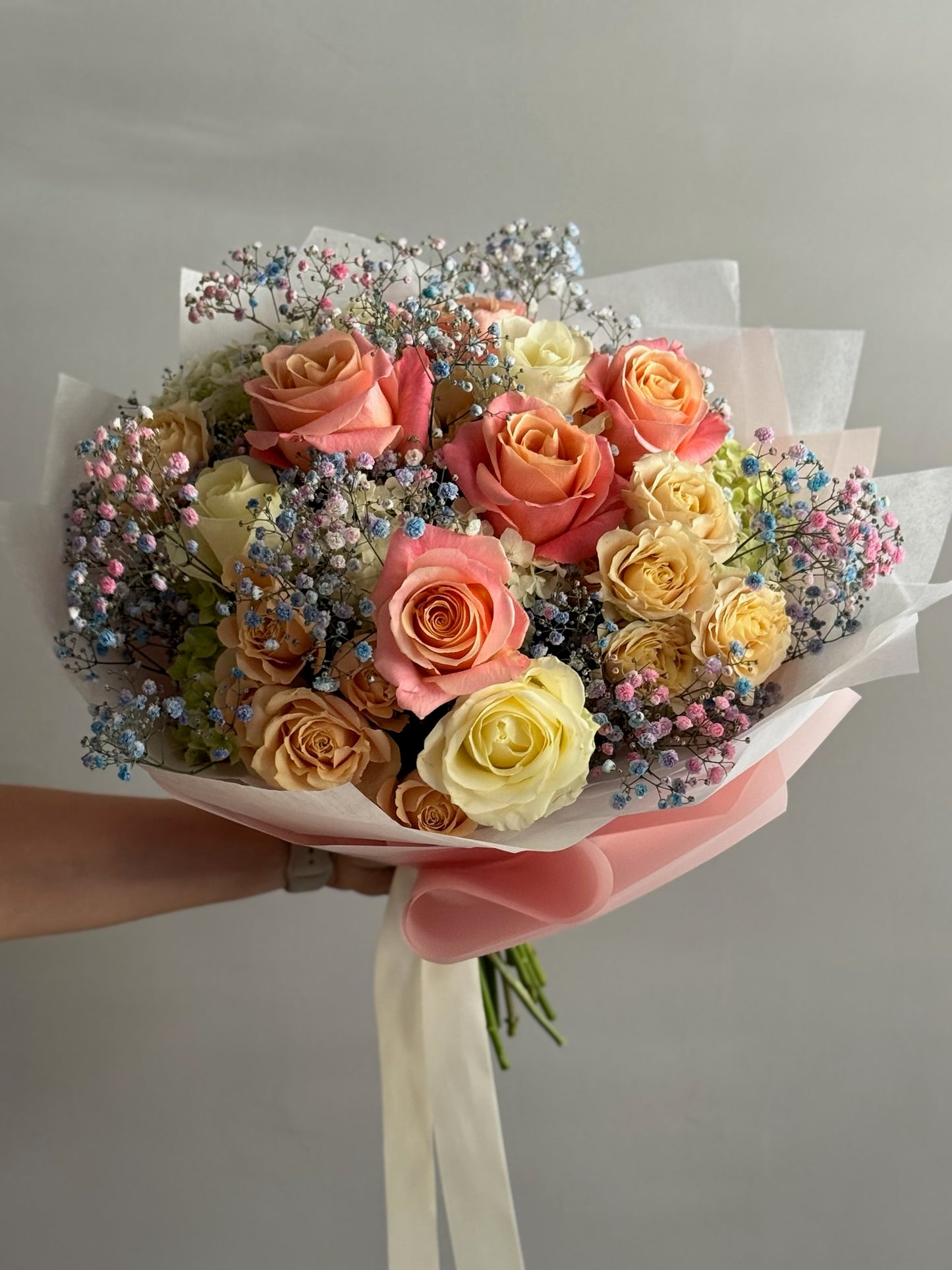 Bouquet of multicolored roses with decorative elements held by a person against a neutral background