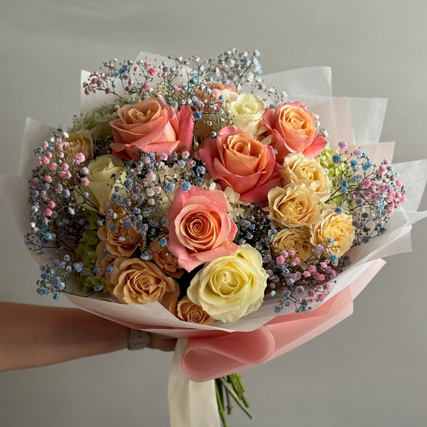 Bouquet of multicolored roses with decorative elements held by a person against a neutral background