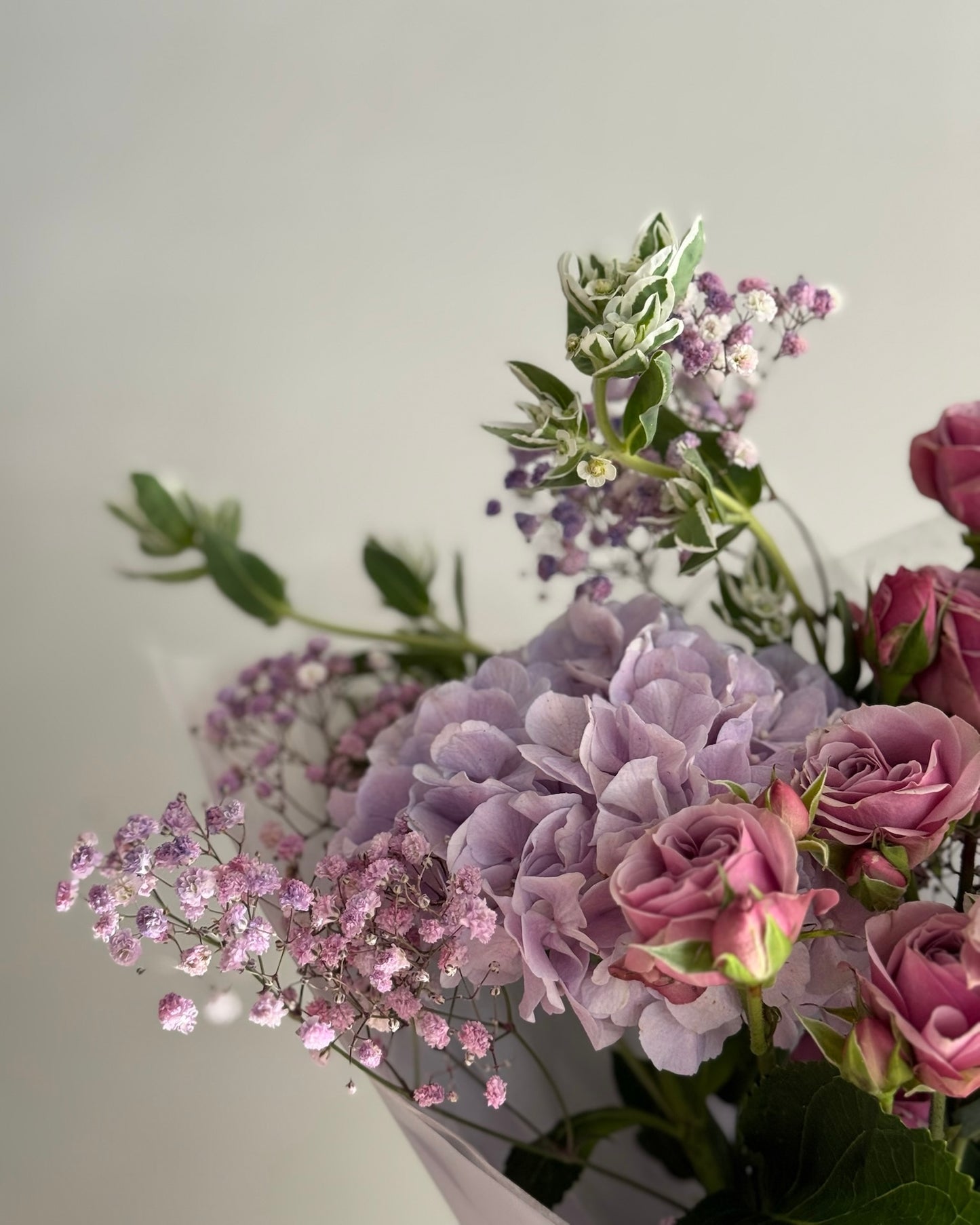 Bouquet of purple and pink flowers with greenery on a light gray background