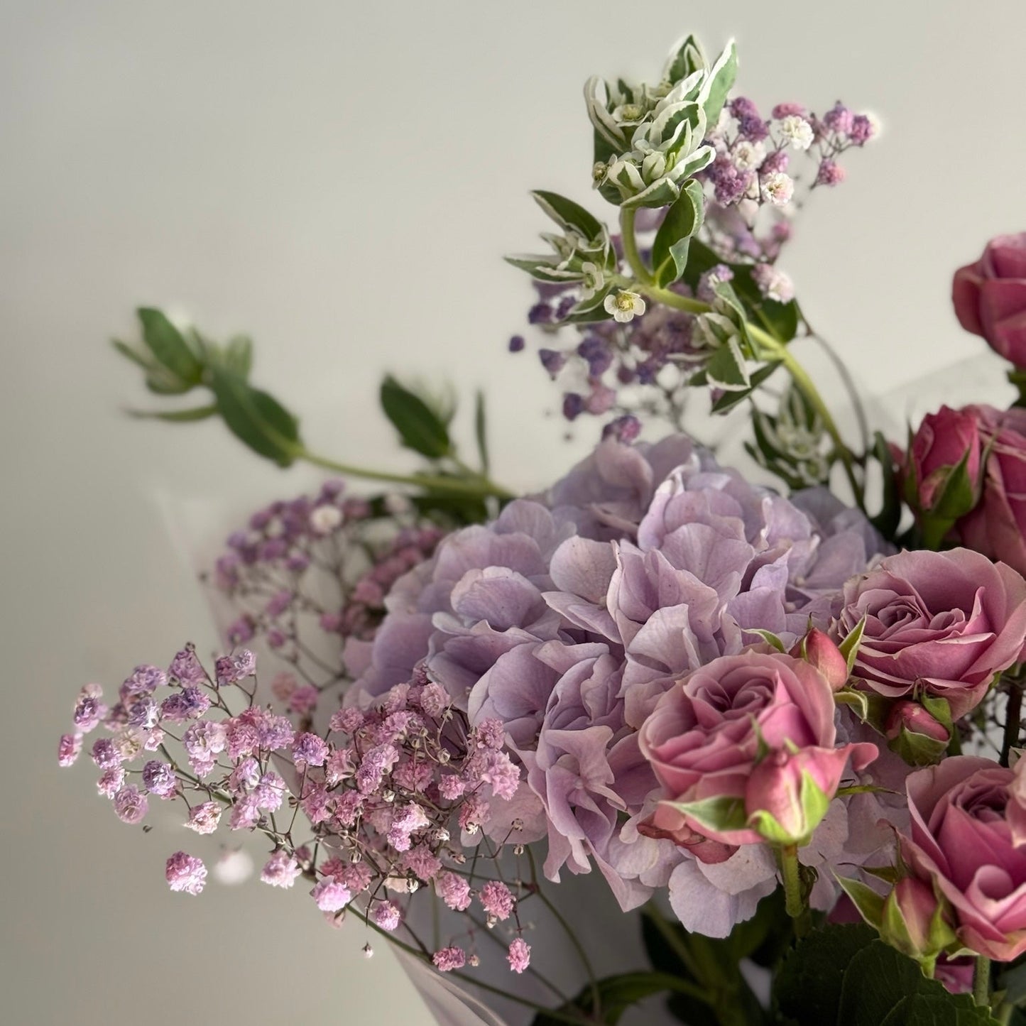 Bouquet of purple and pink flowers with greenery on a light gray background
