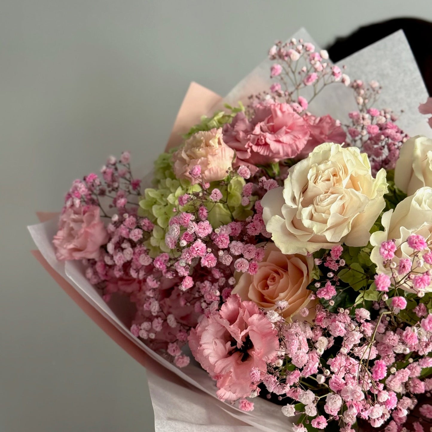 Bouquet of pink and white flowers held against a neutral background