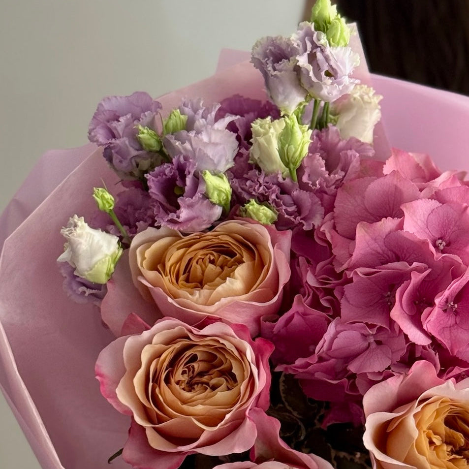 Bouquet of flowers with pink, purple, and beige colors in a pink wrap.