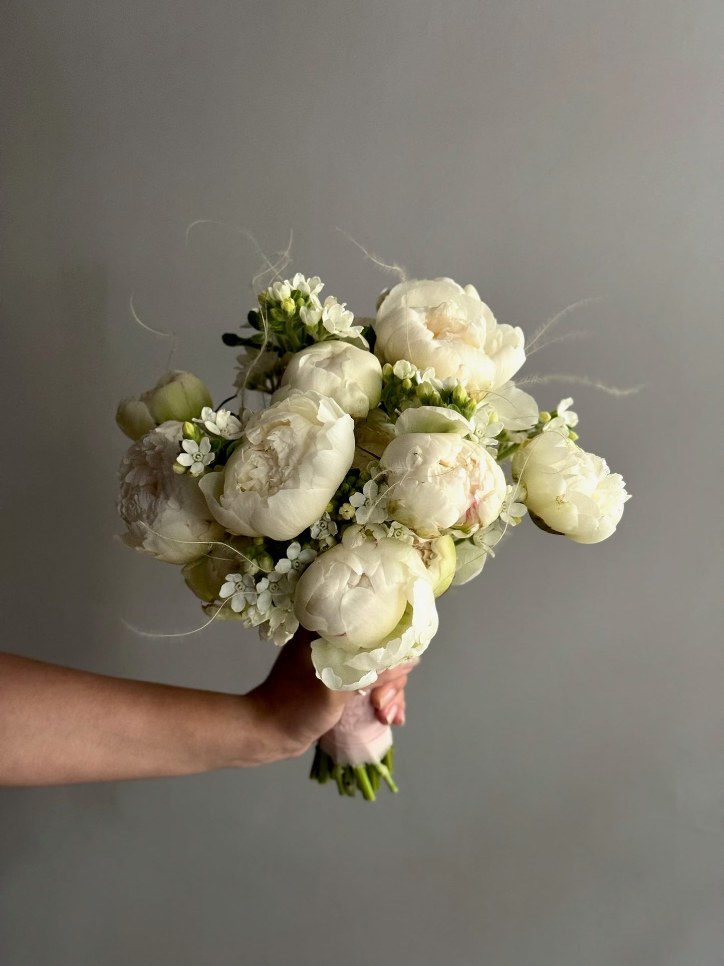 Bouquet of white flowers held against a gray background