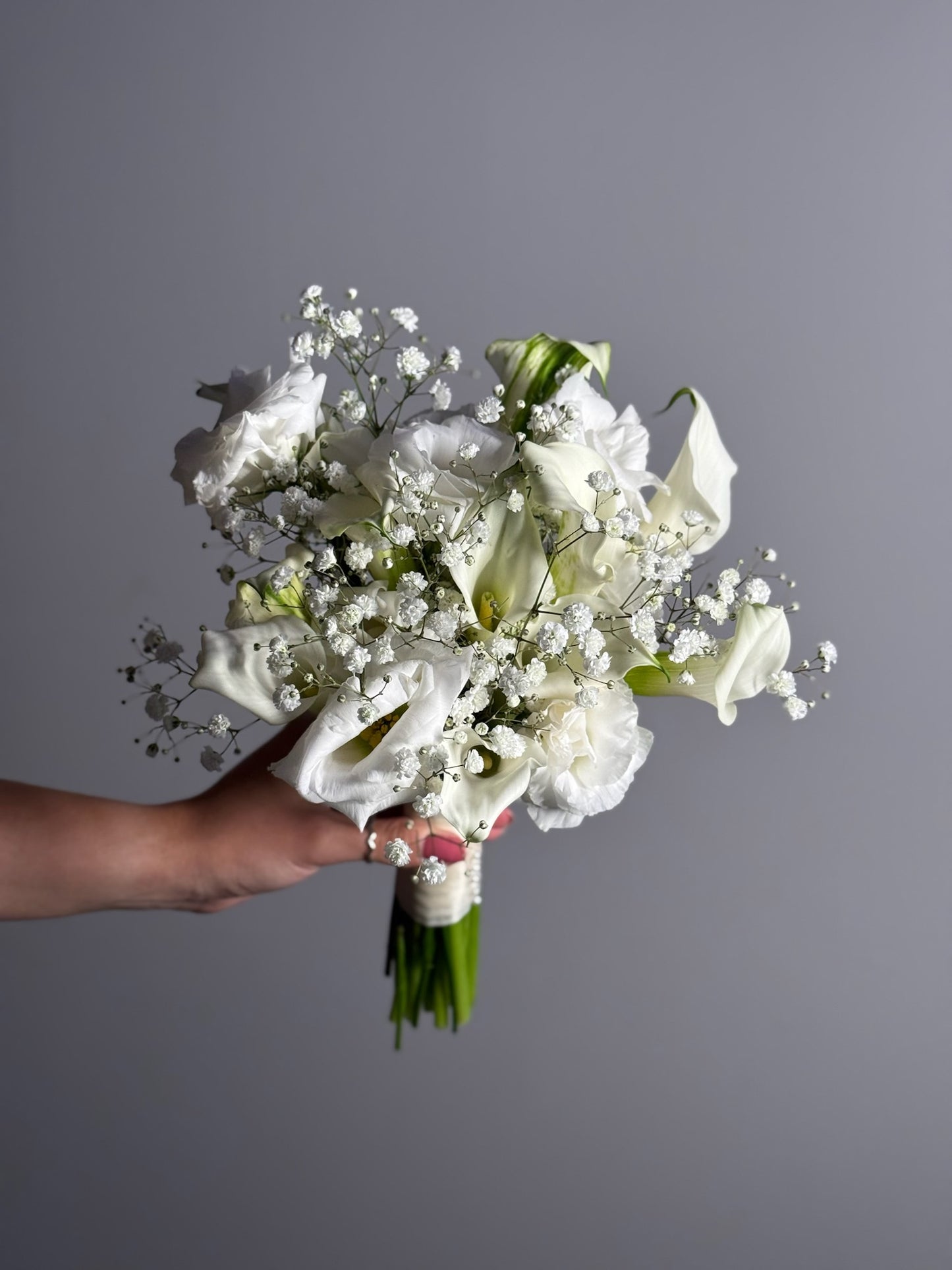 Bouquet of white flowers held by a hand against a gray background
