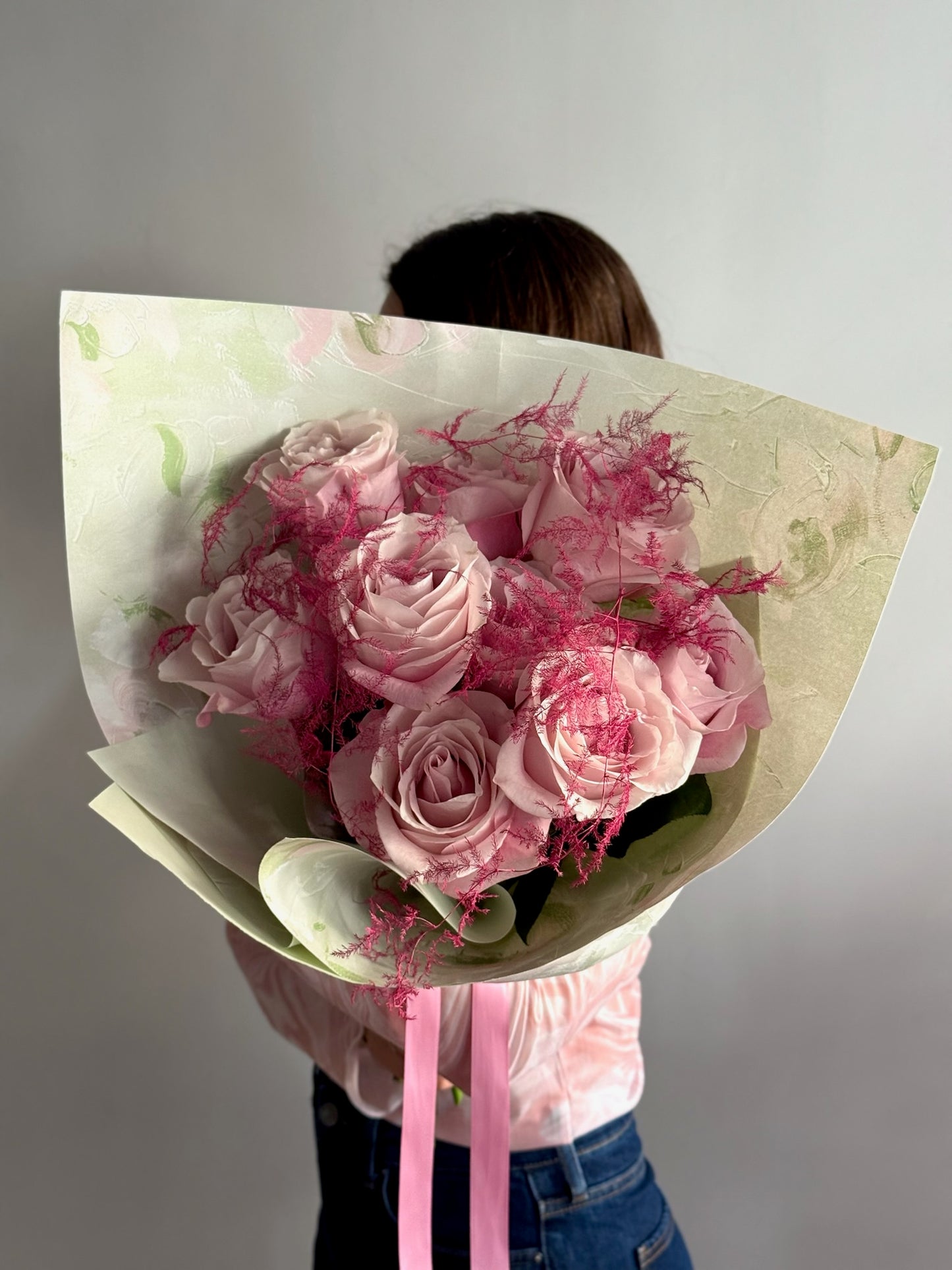 Person holding a bouquet of pink roses wrapped in paper against a plain background