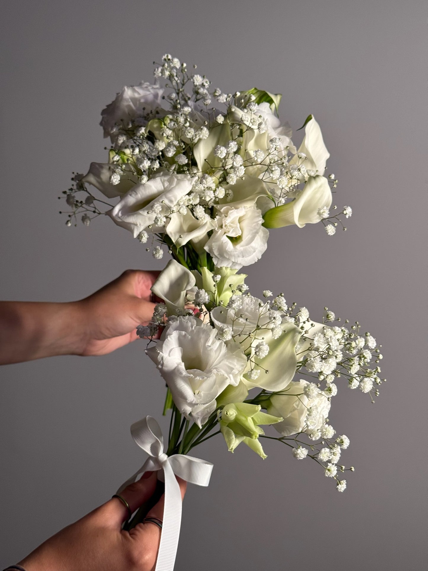 Bouquet of white flowers held by a hand against a gray background