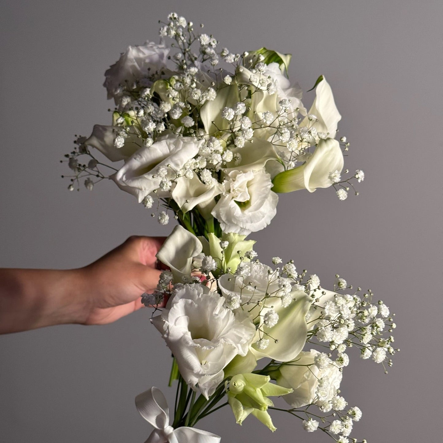 Bouquet of white flowers held by a hand against a gray background