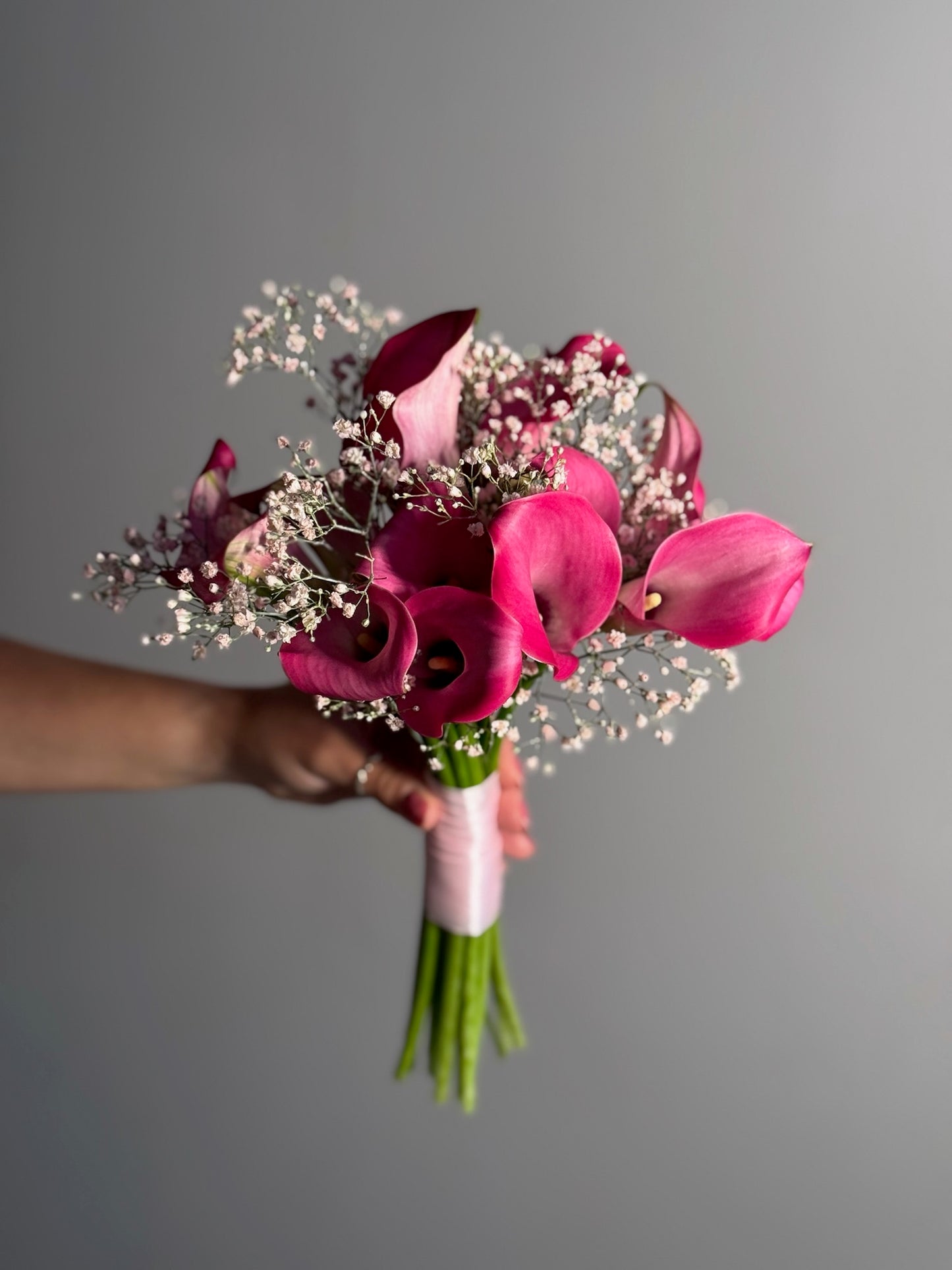 Bouquet of pink flowers held by a hand against a gray background