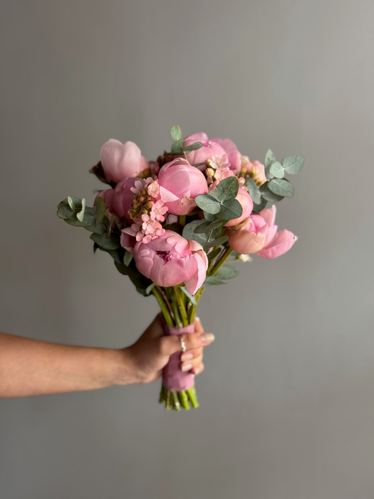 Bouquet of pink flowers held by a hand against a gray background