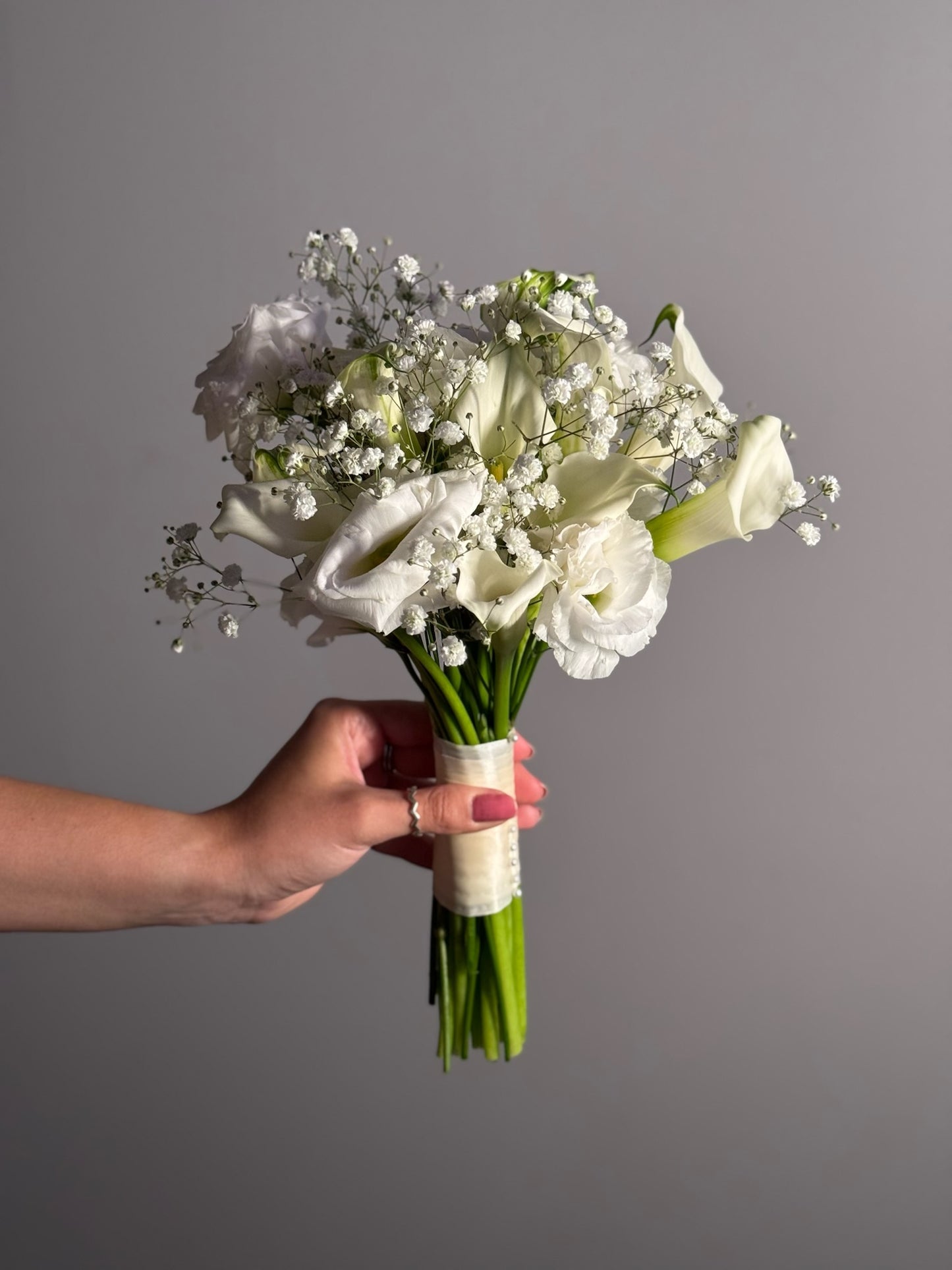 Hand holding a bouquet of white flowers against a gray background