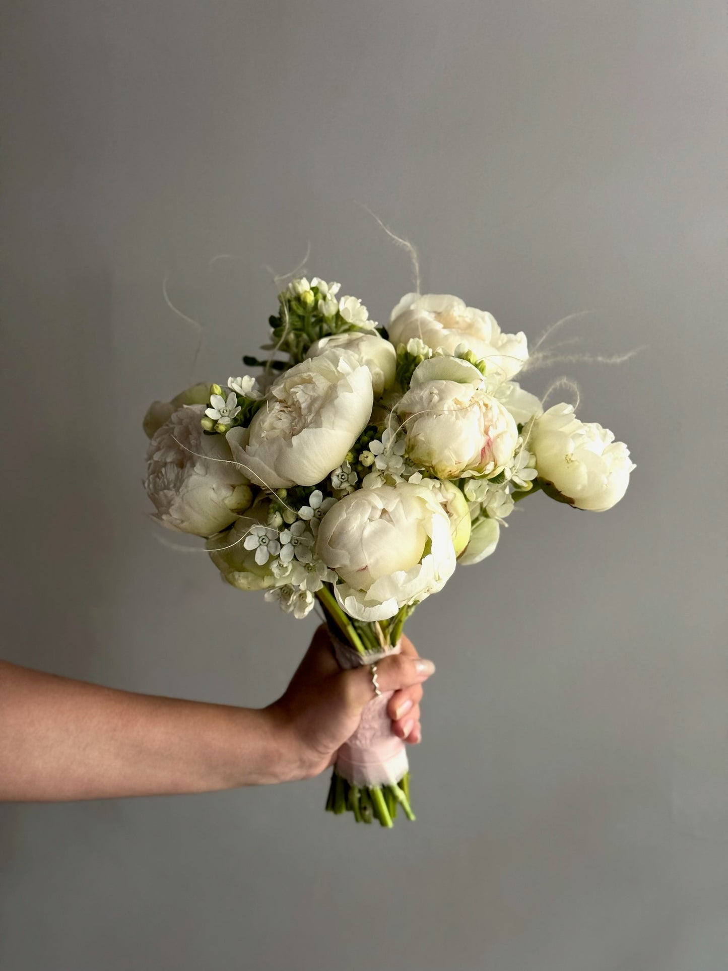 Bouquet of white flowers held by a hand against a gray background