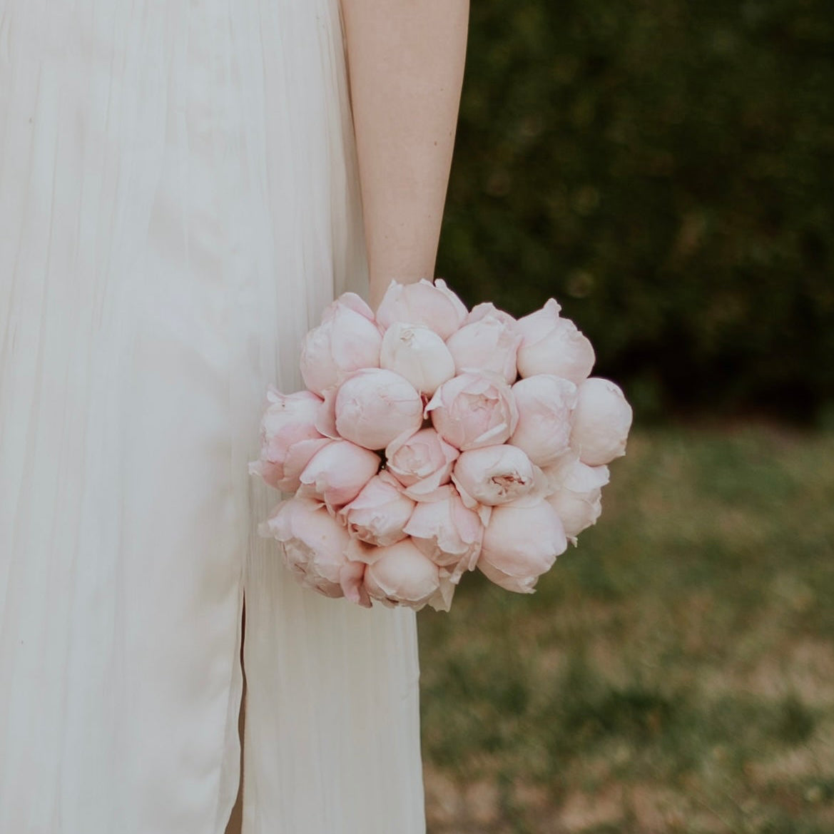 Bride holding a bouquet of pink flowers with a blurred natural background