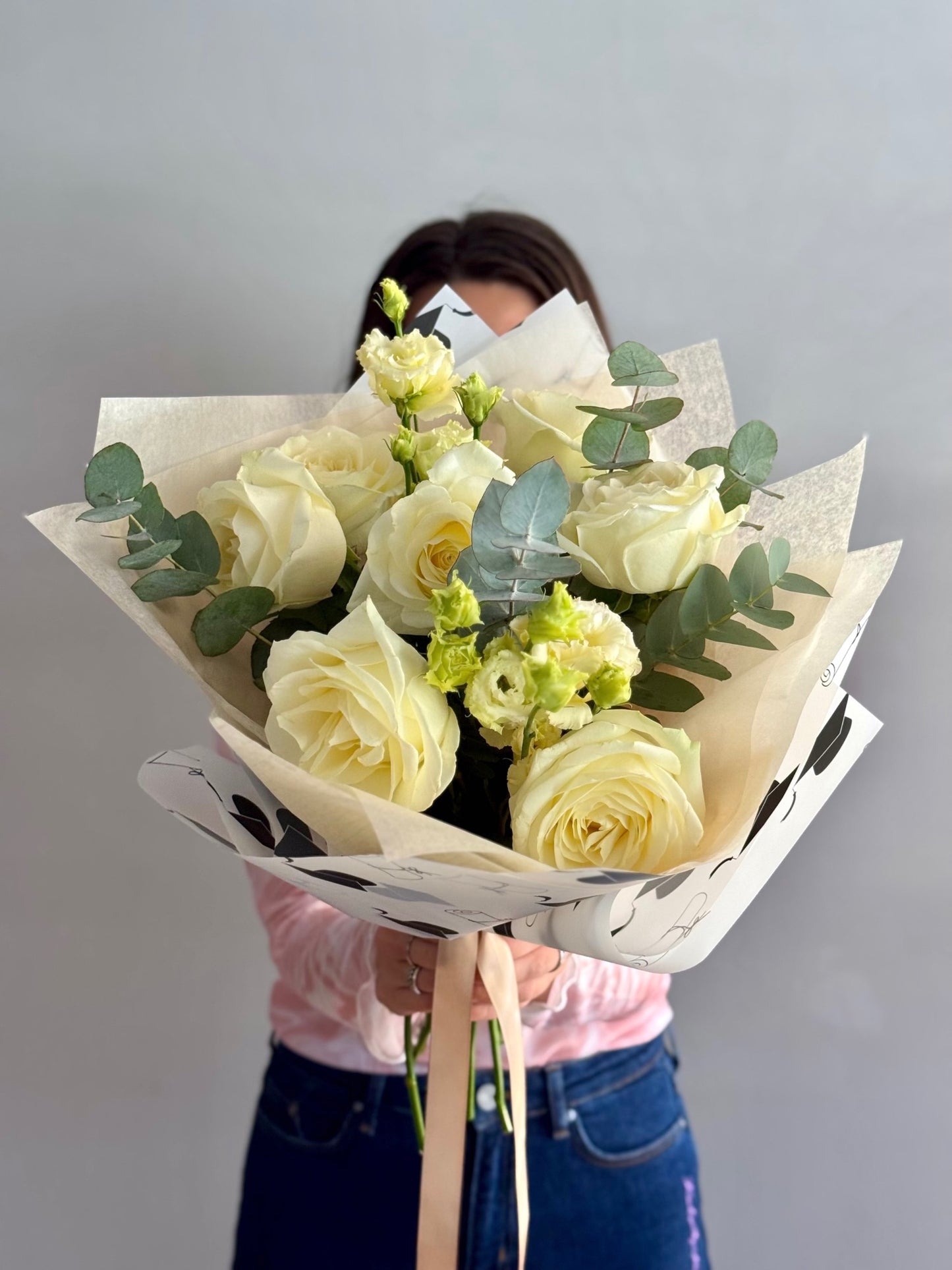 Bouquet of white roses with greenery held by a person against a plain background