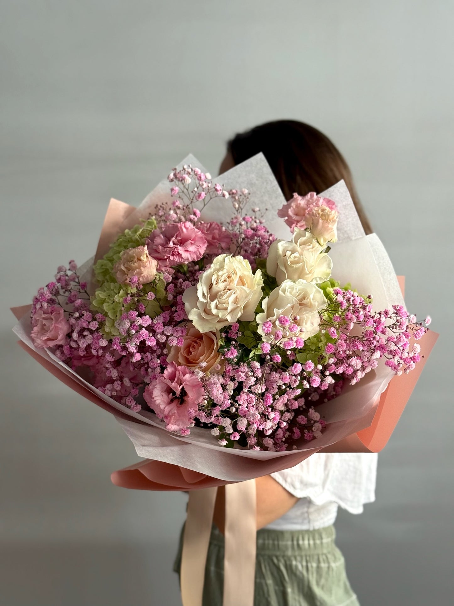Person holding a bouquet of pink and white flowers against a plain background