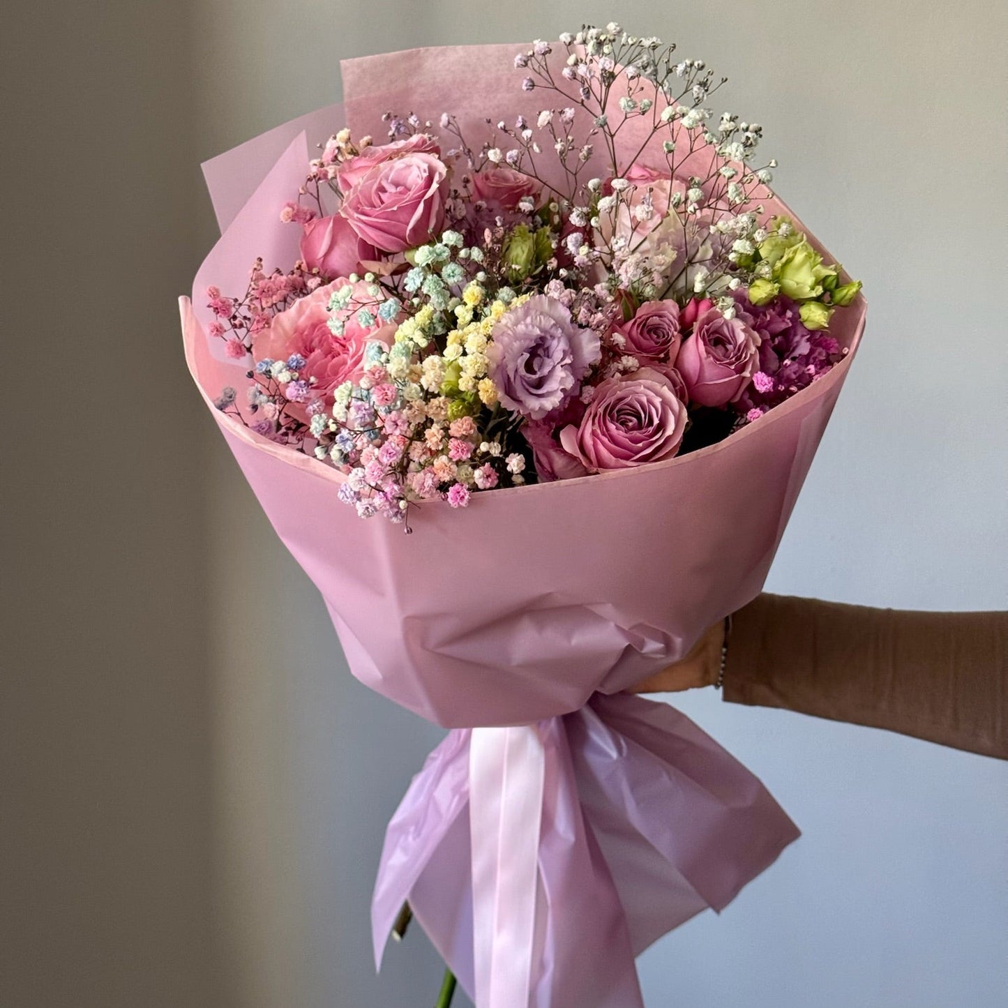 Bouquet of pink and purple flowers wrapped in pink paper held against a neutral background