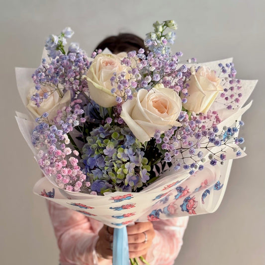 Person holding a bouquet of flowers wrapped in colorful paper against a plain background