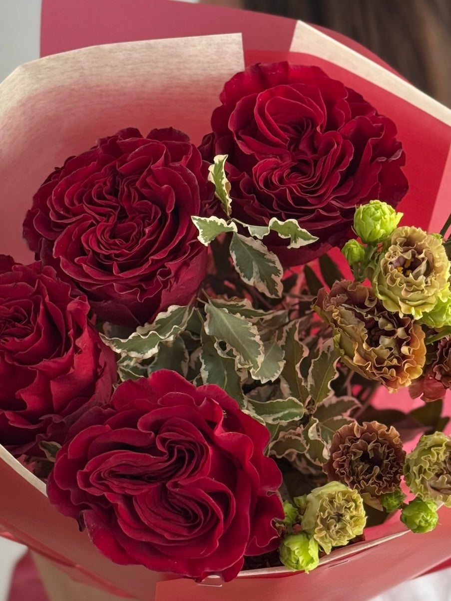 Bouquet of red and green flowers in a box with a pink background