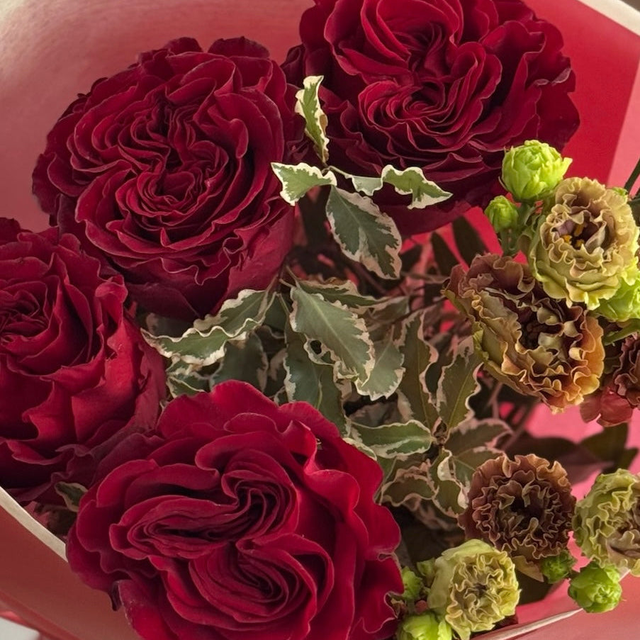 Bouquet of red and green flowers in a box with a pink background