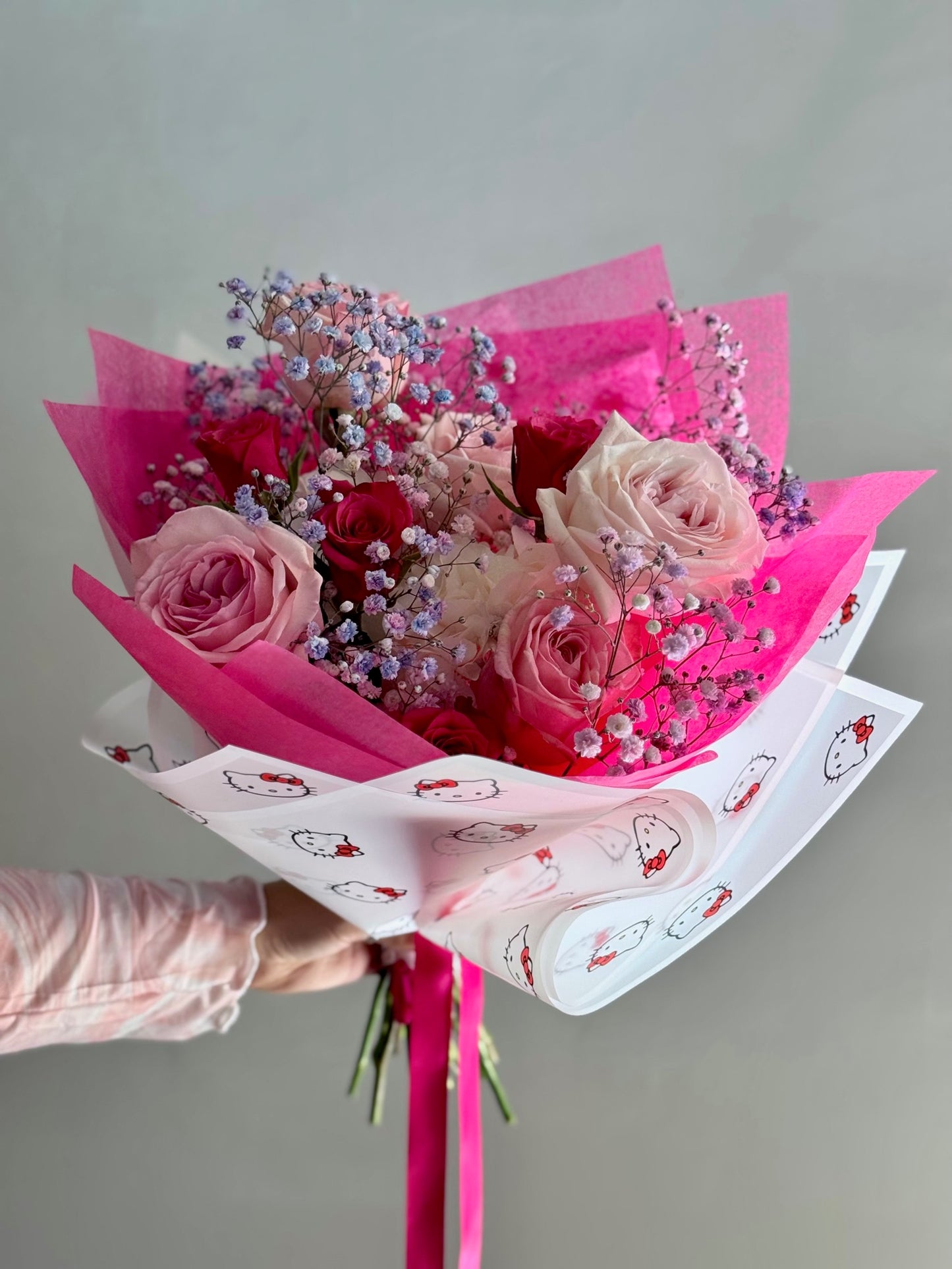 Bouquet of pink roses with pink wrapping paper held by a person against a gray background