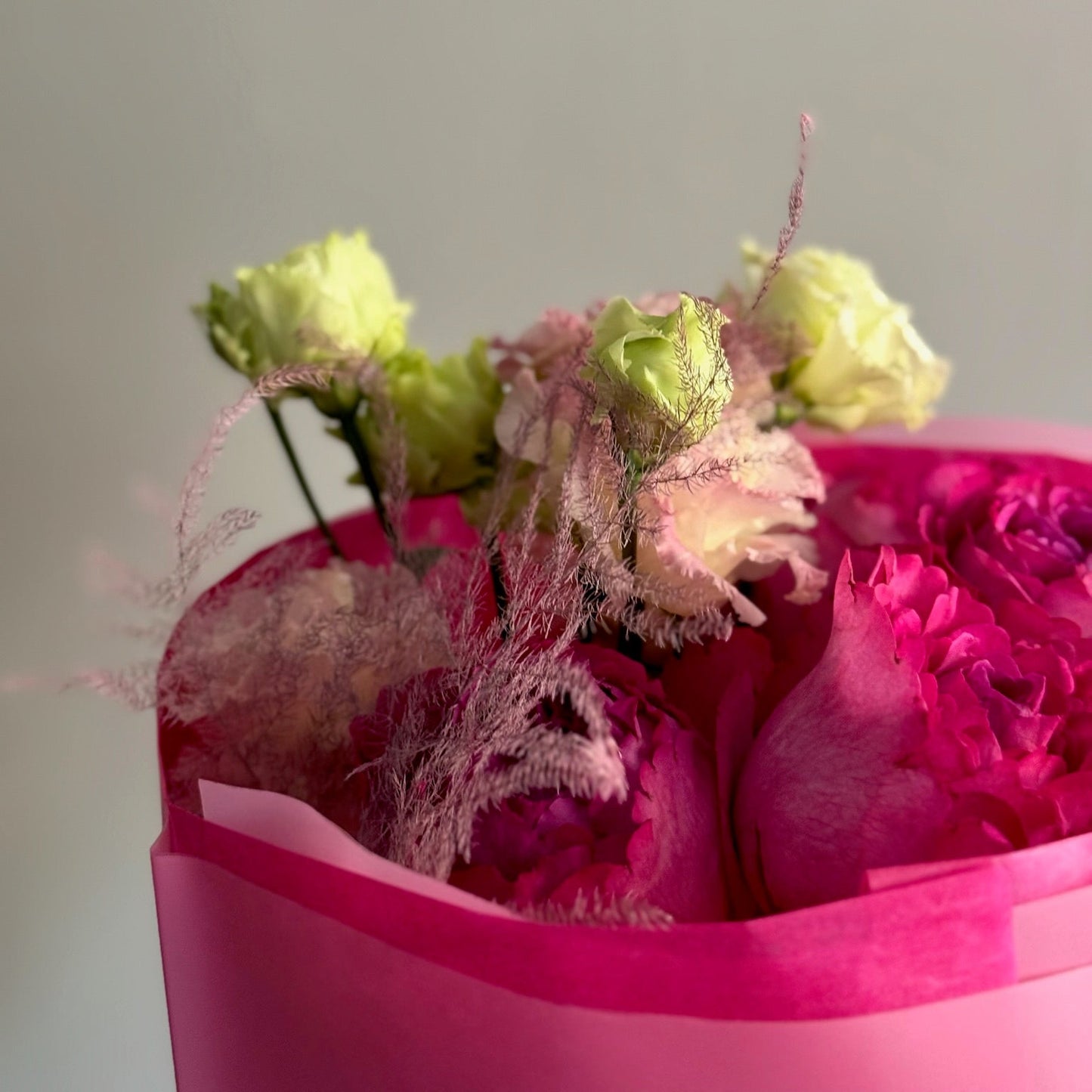 Pink heart-shaped box filled with flowers on a light gray background