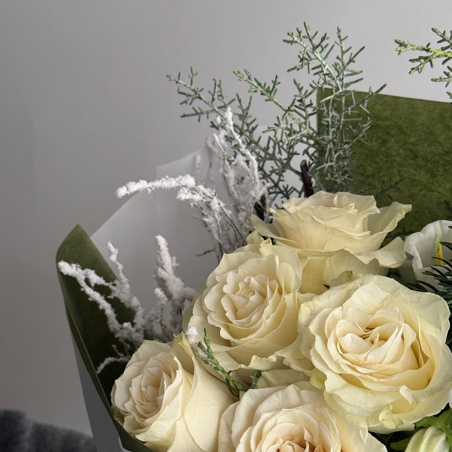 Bouquet of white roses with greenery in a clear wrap against a neutral background