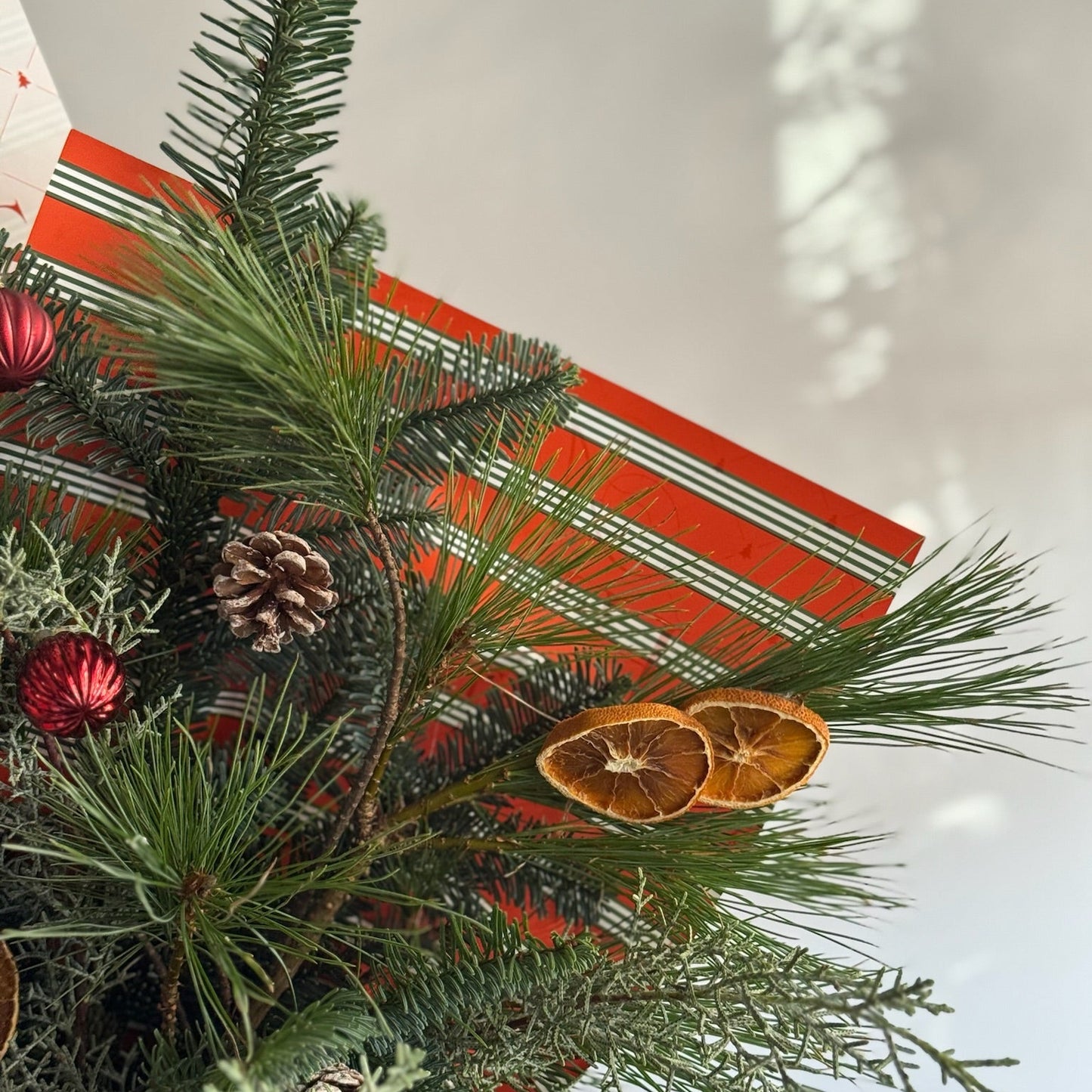 Decorative Christmas arrangement with greenery, pinecones, and dried oranges on a striped fabric background.