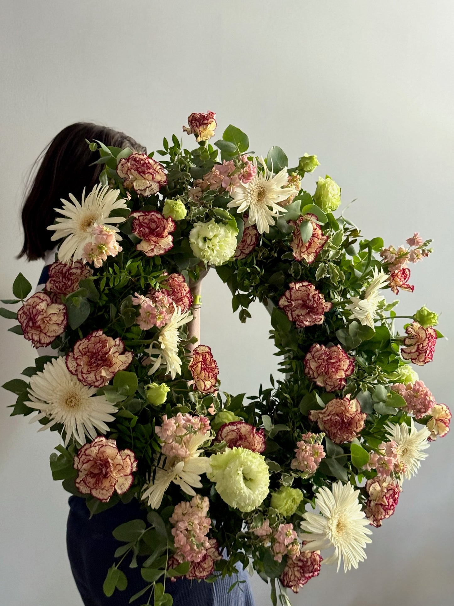 Floral wreath with a person holding it against a plain background