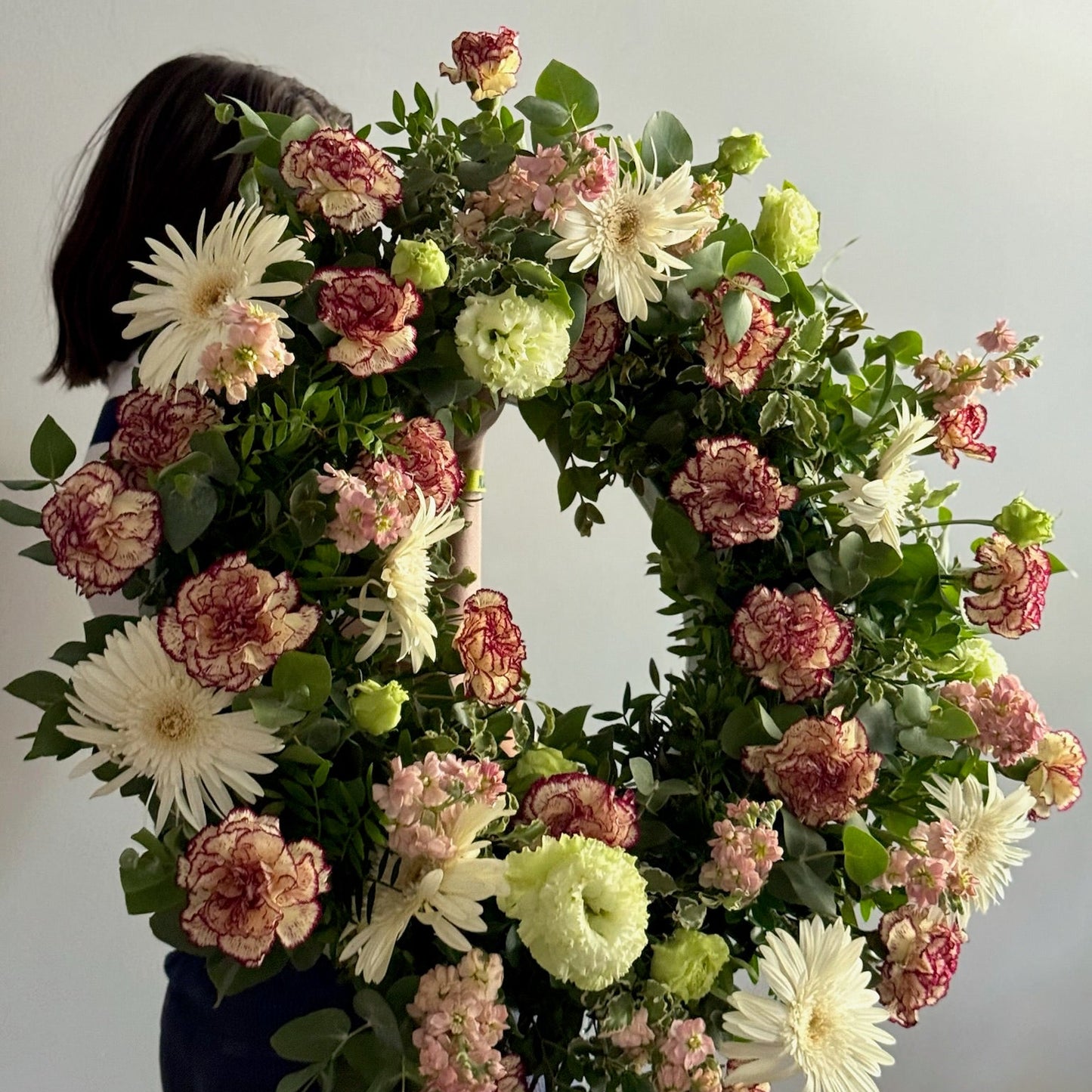 Floral wreath with a person holding it against a plain background