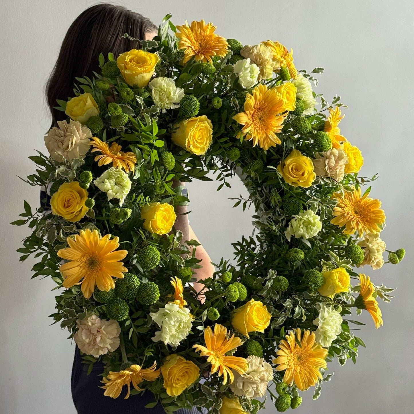 Person holding a floral wreath with yellow and white flowers against a plain background