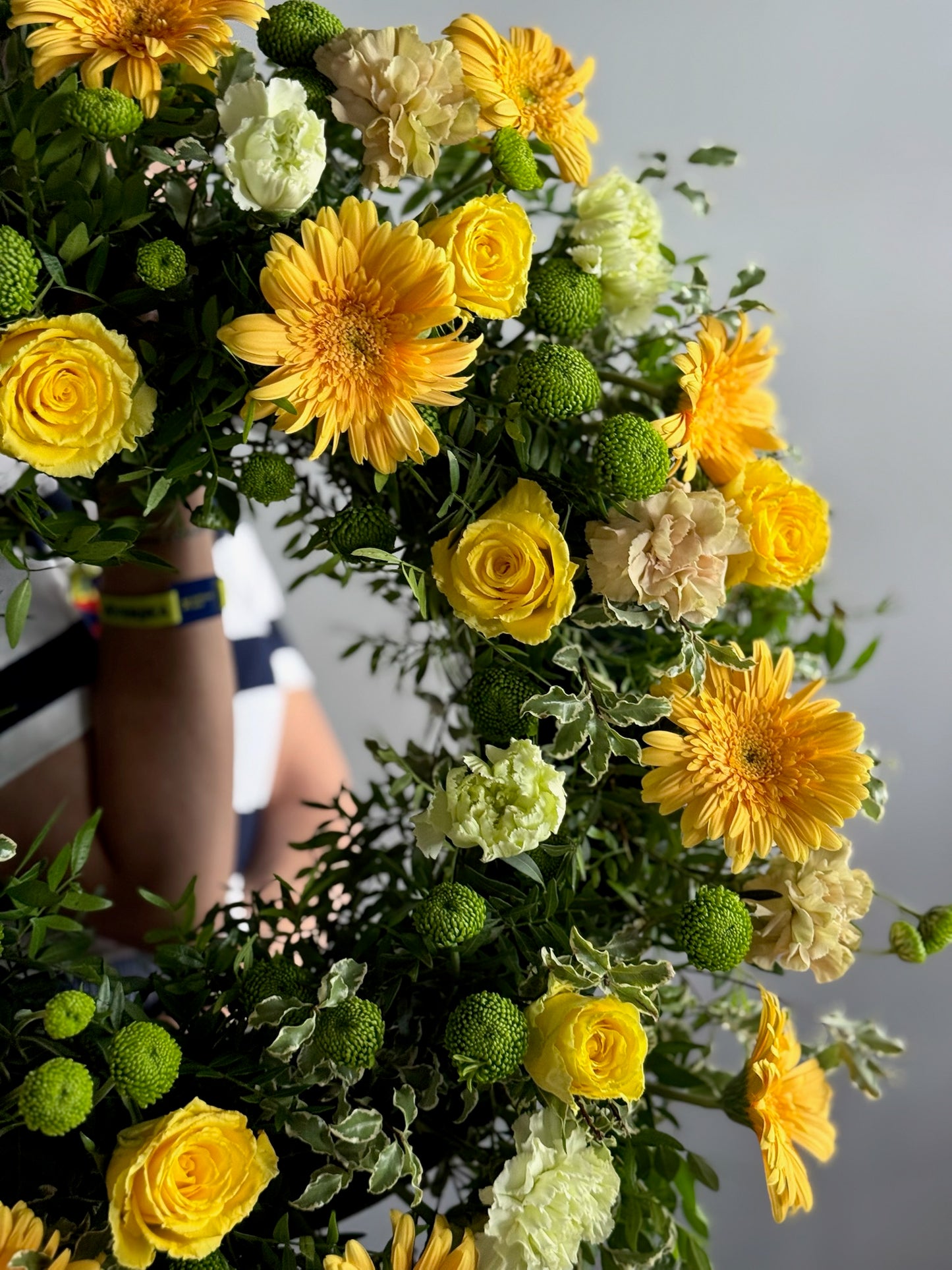 Bouquet of yellow and green flowers held by a person against a neutral background
