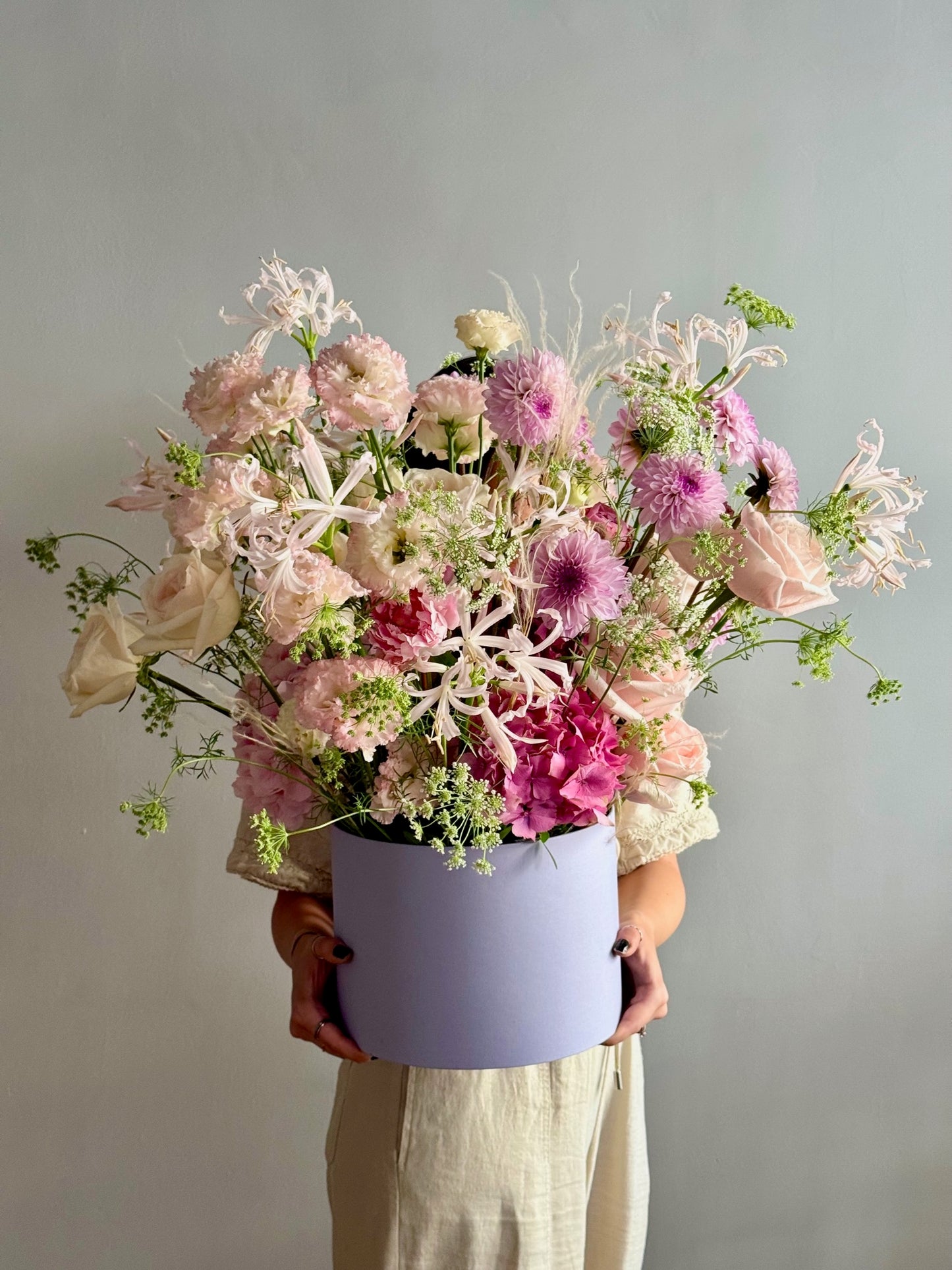 Person holding a bouquet of flowers in a light purple box against a plain background