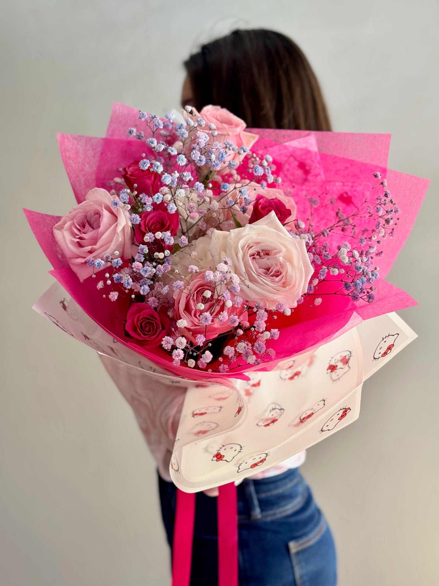 Person holding a bouquet of pink and white flowers wrapped in pink paper with a Hello Kitty design.