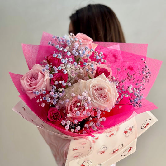 Person holding a bouquet of pink and white flowers wrapped in pink paper with a Hello Kitty design.
