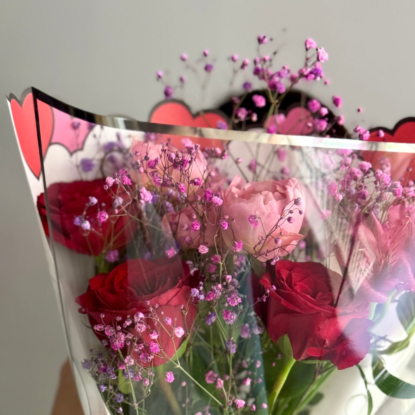 Bouquet of red roses and pink flowers with decorative paper in the foreground