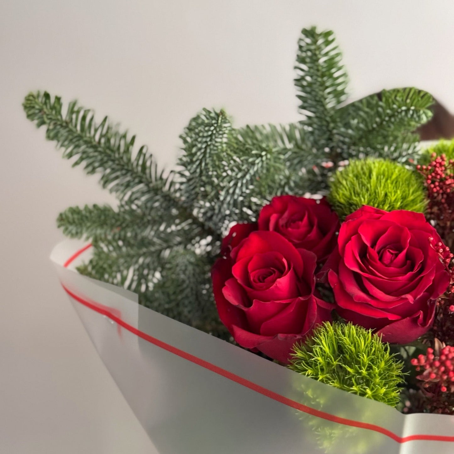 Bouquet of red roses with greenery in a white box with red ribbon on a light gray background