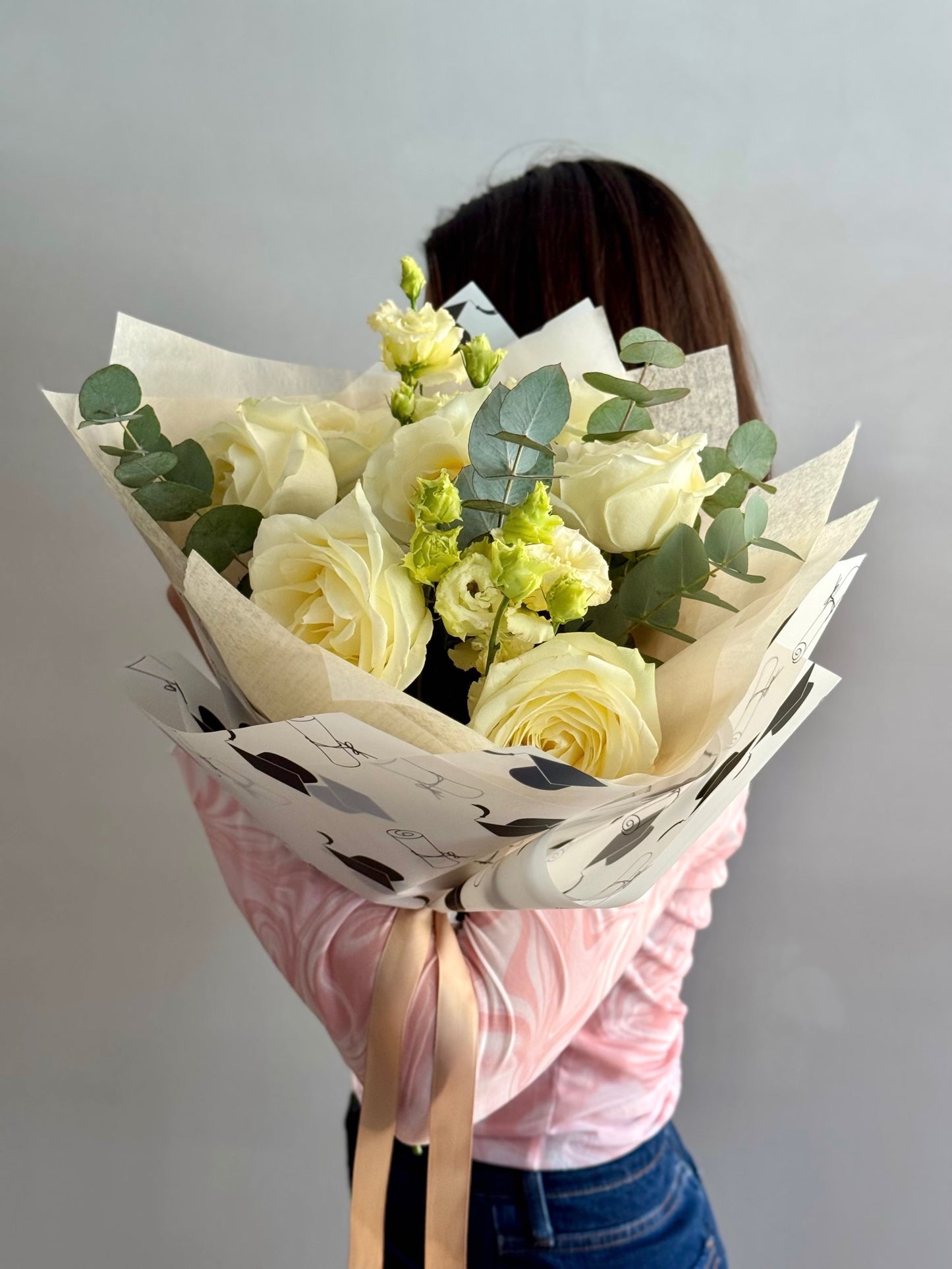 Person holding a bouquet of white and yellow roses with greenery against a plain background