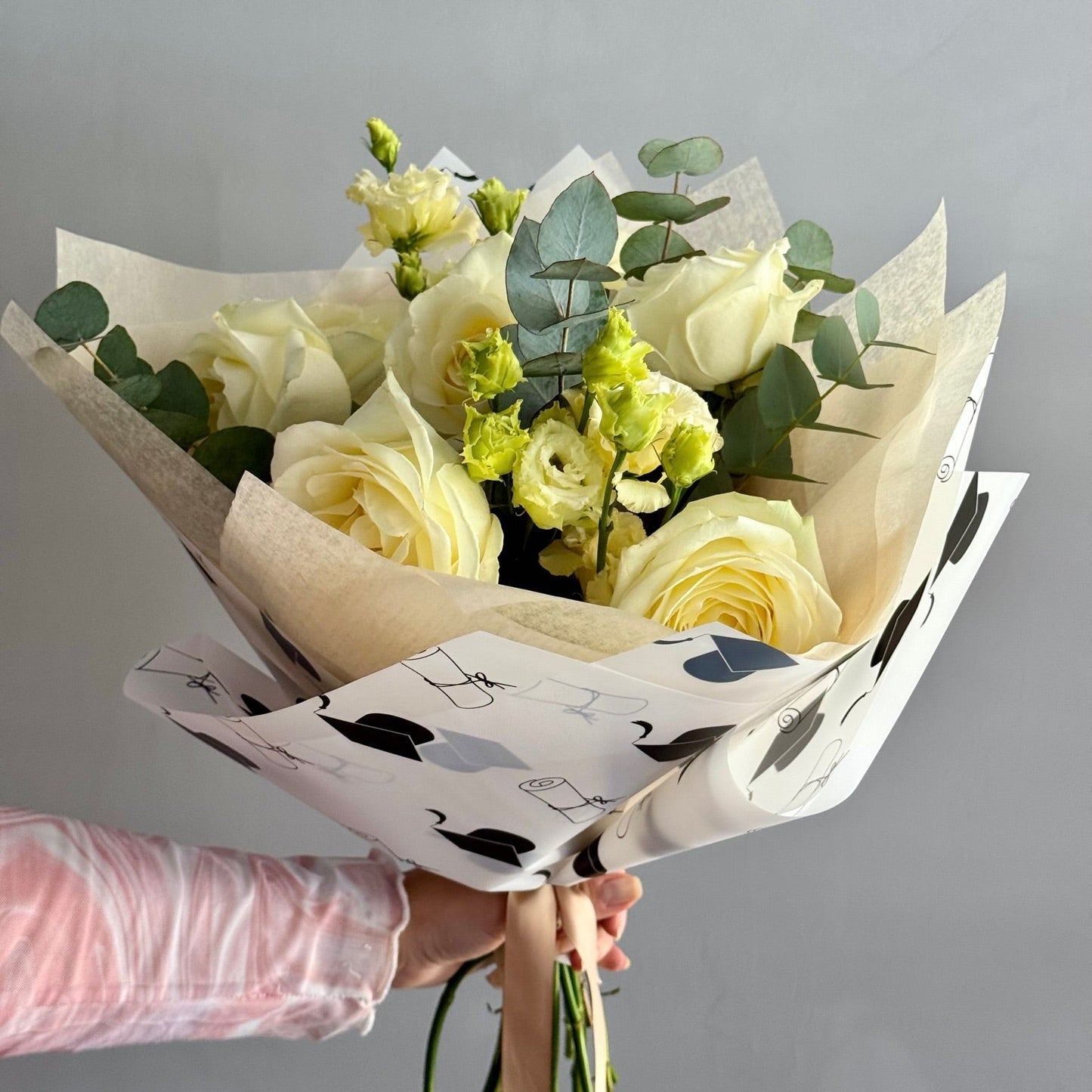 Bouquet of white and green flowers wrapped in paper with black patterns, held by a person.