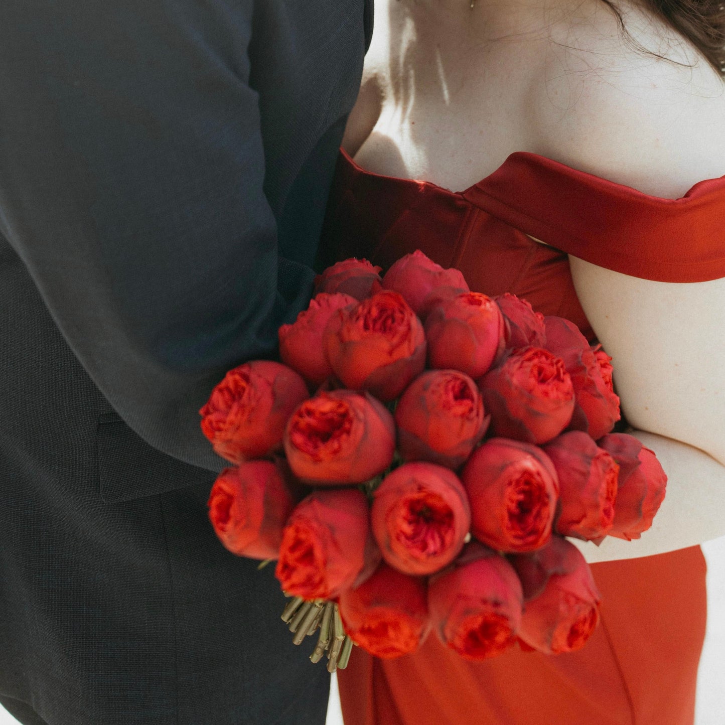 Person in a red dress holding a bouquet of red roses, with a blurred background