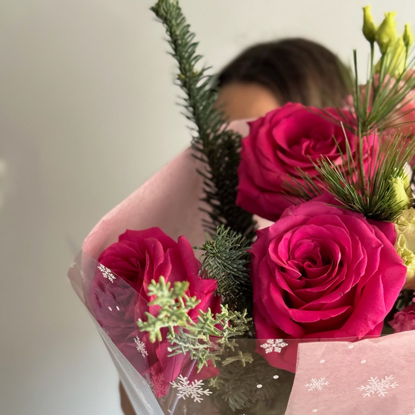 Bouquet of pink roses with greenery held by a person against a neutral background